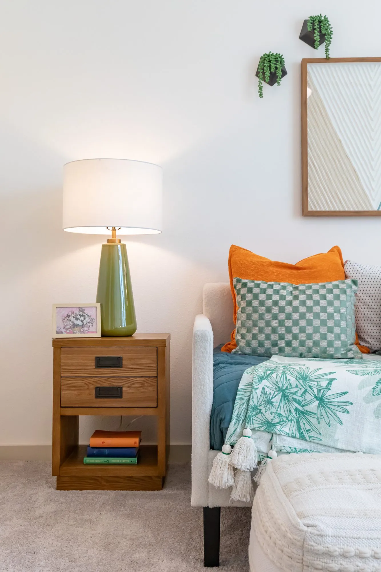 Multifamily apartment bedroom corner with a green ceramic lamp on a wood nightstand beside a daybed with checked pillows
