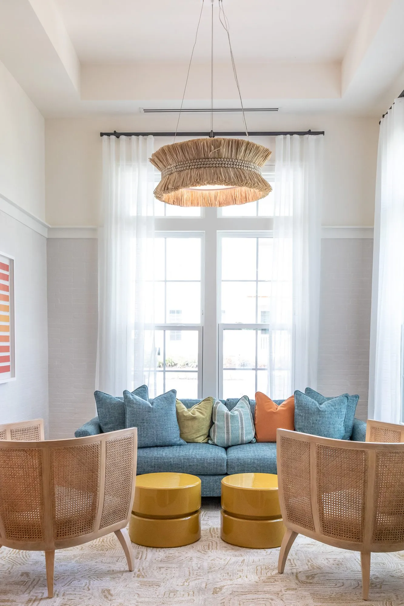 Multifamily sitting room with a blue sofa between sheer curtained windows under a fringed rattan pendant