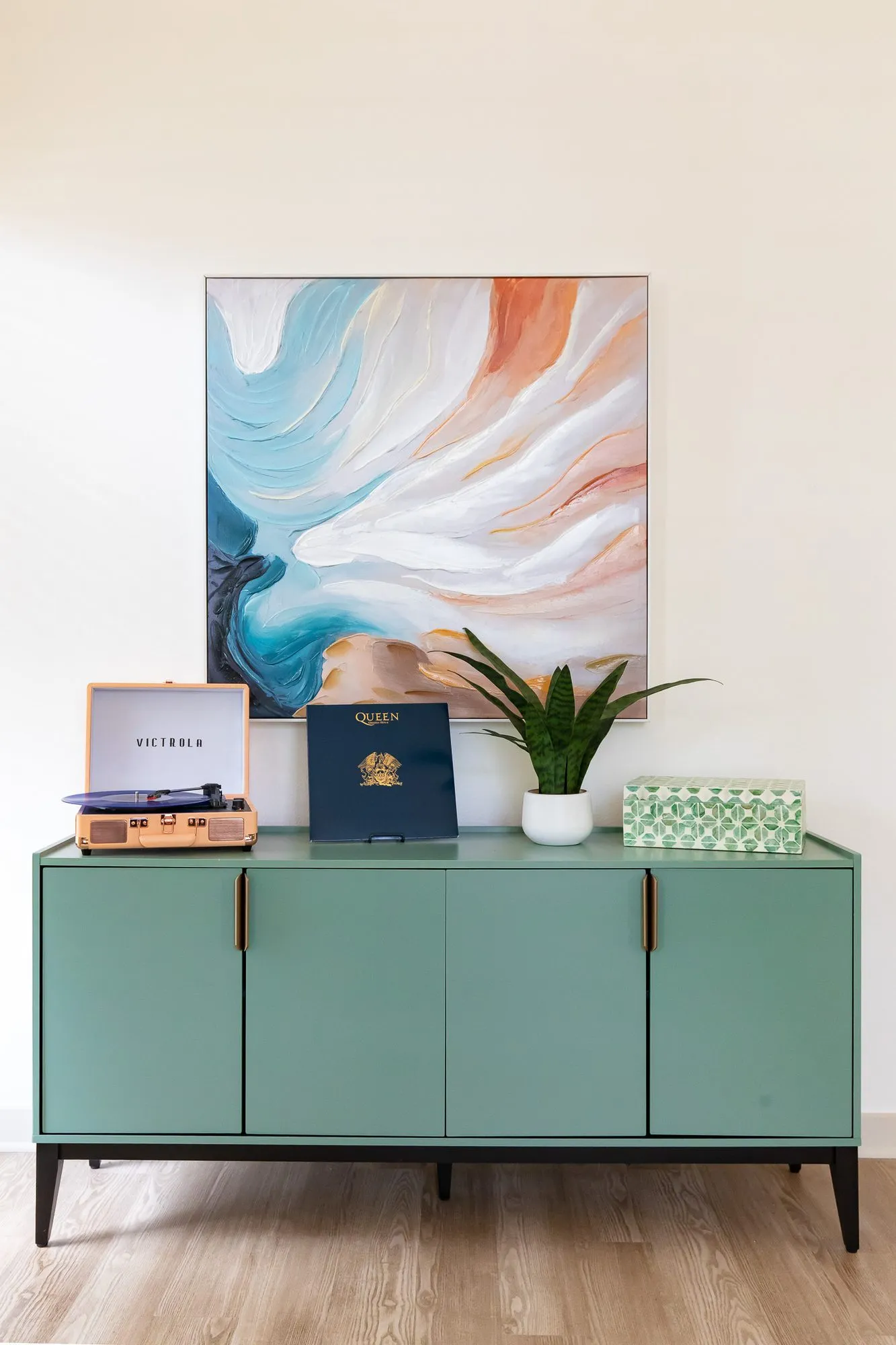 Multifamily interior detail: green sideboard with a record player, books and a plant below an abstract painting