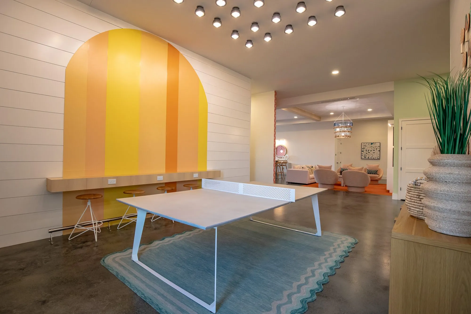Multifamily amenity ping pong table on a blue zigzag rug before a striped yellow and orange arch, the lounge beyond