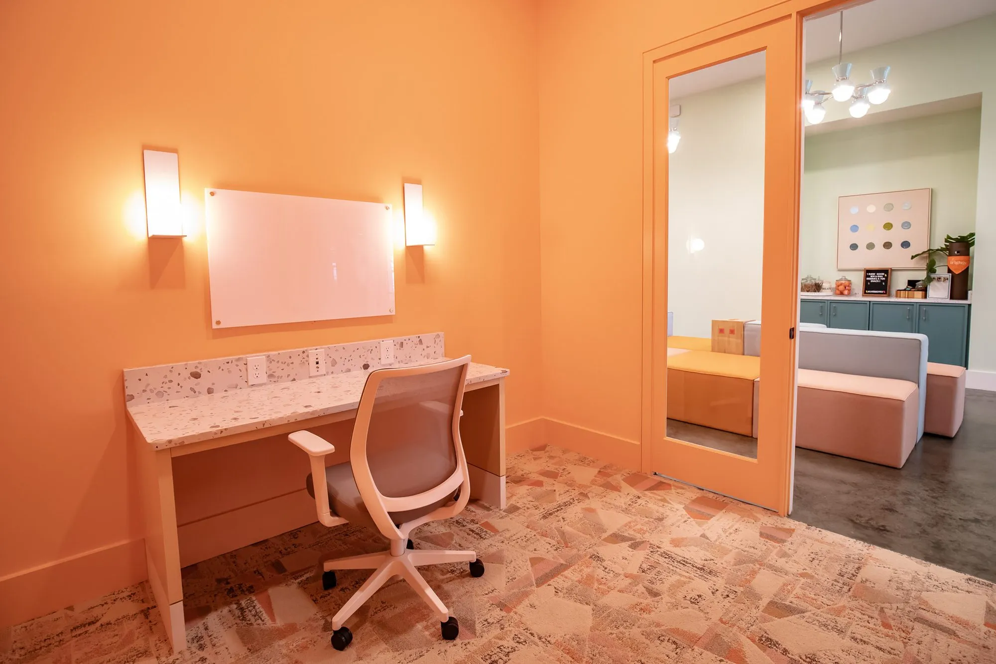 Multifamily amenity study room painted orange with a white desk, task chair, whiteboard and sconces over a newsprint floor