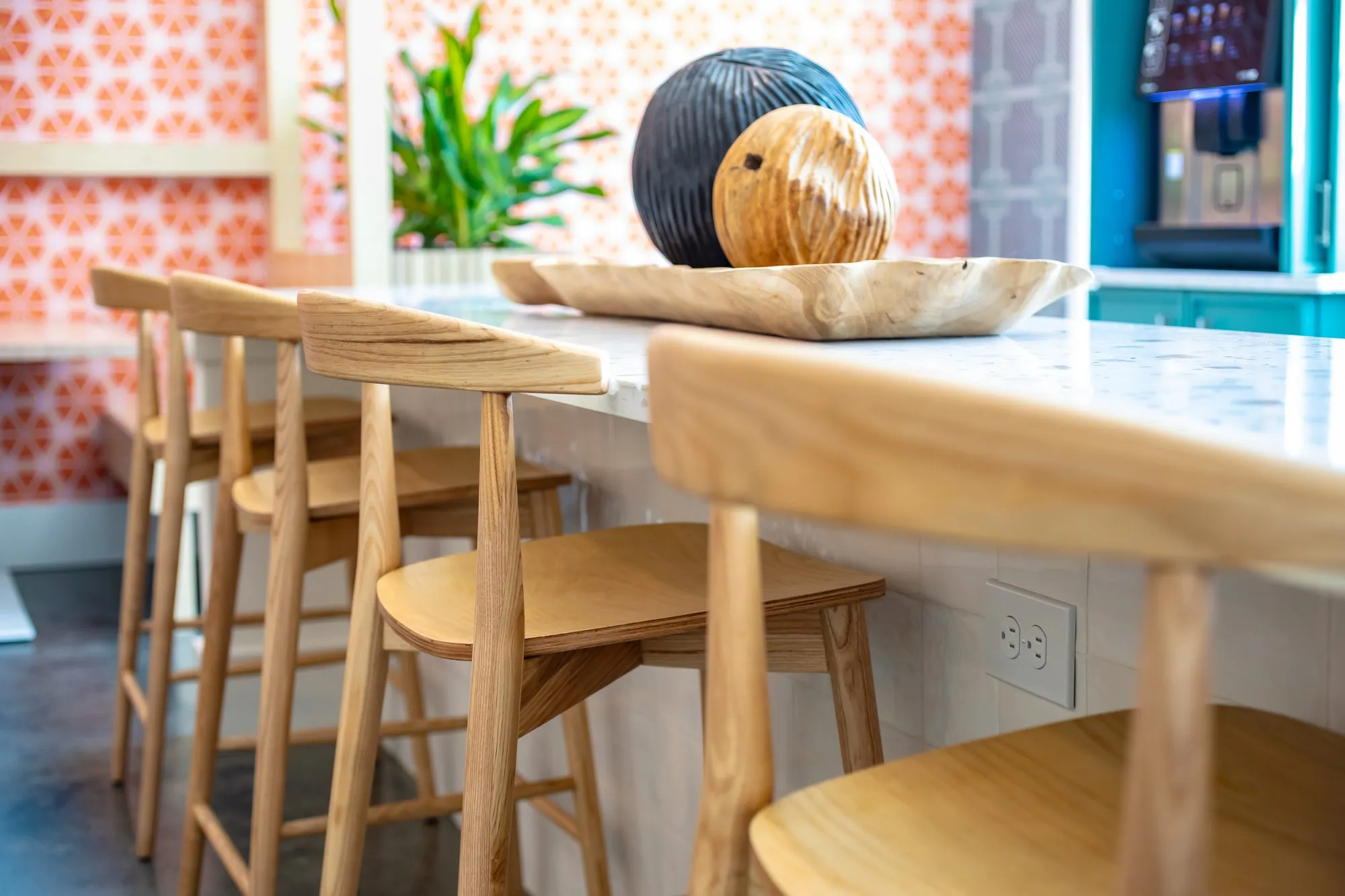 Multifamily interior detail: blond wood barstools along a terrazzo counter with spheres on a tray, citrus wallpaper behind