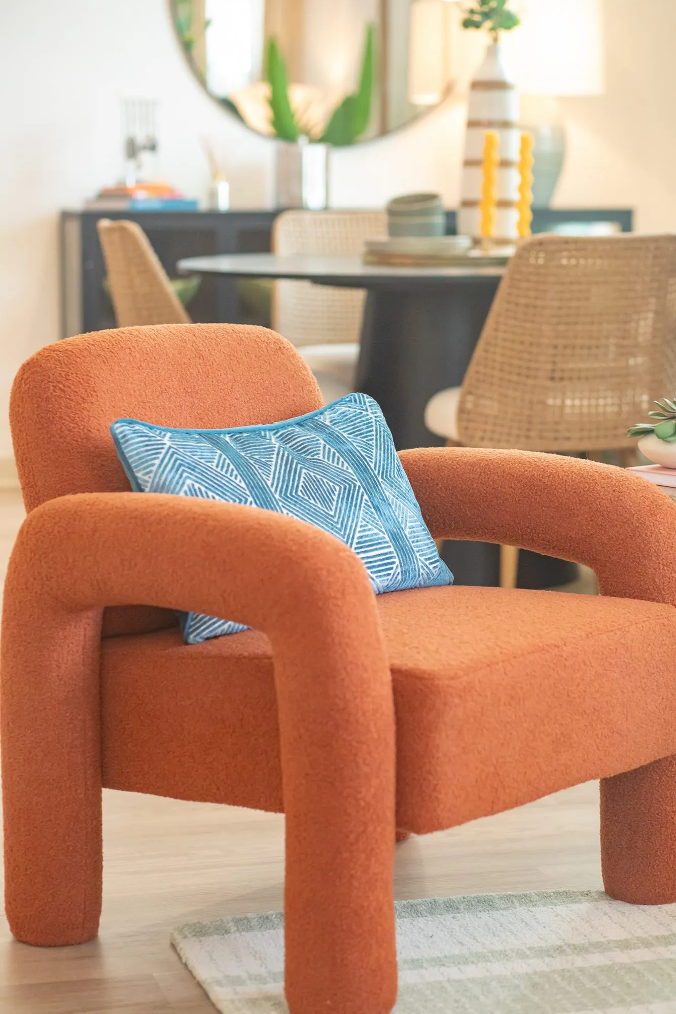 Multifamily interior detail: rust boucle armchair with a blue pillow, a round dining table and cane chairs behind
