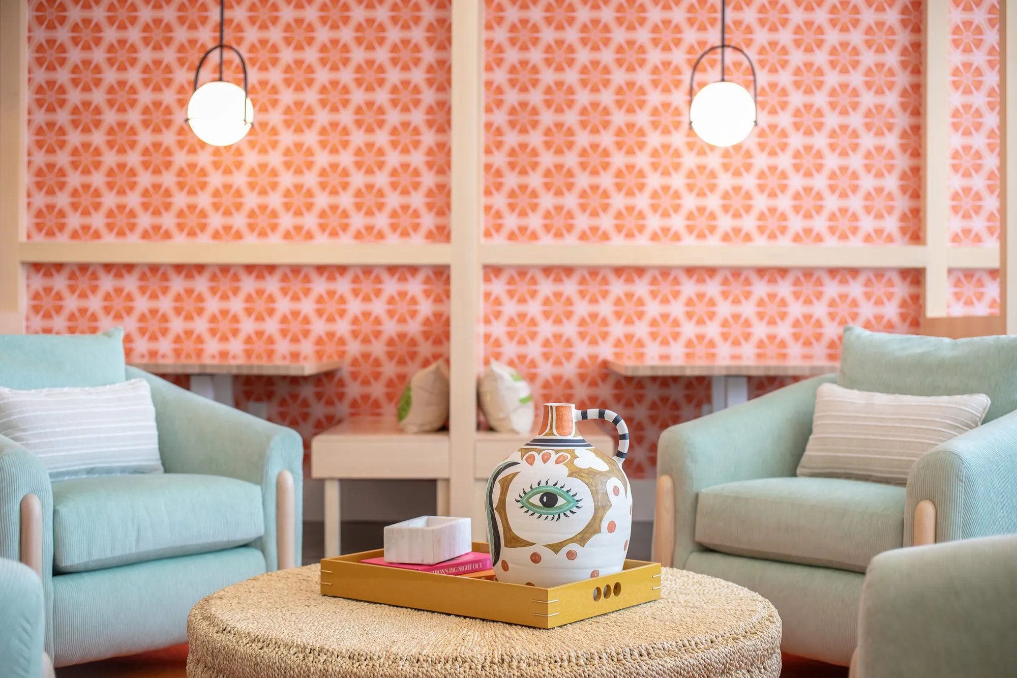Multifamily amenity lounge with mint swivel chairs around a woven ottoman and eye motif pitcher, citrus wallpaper booths