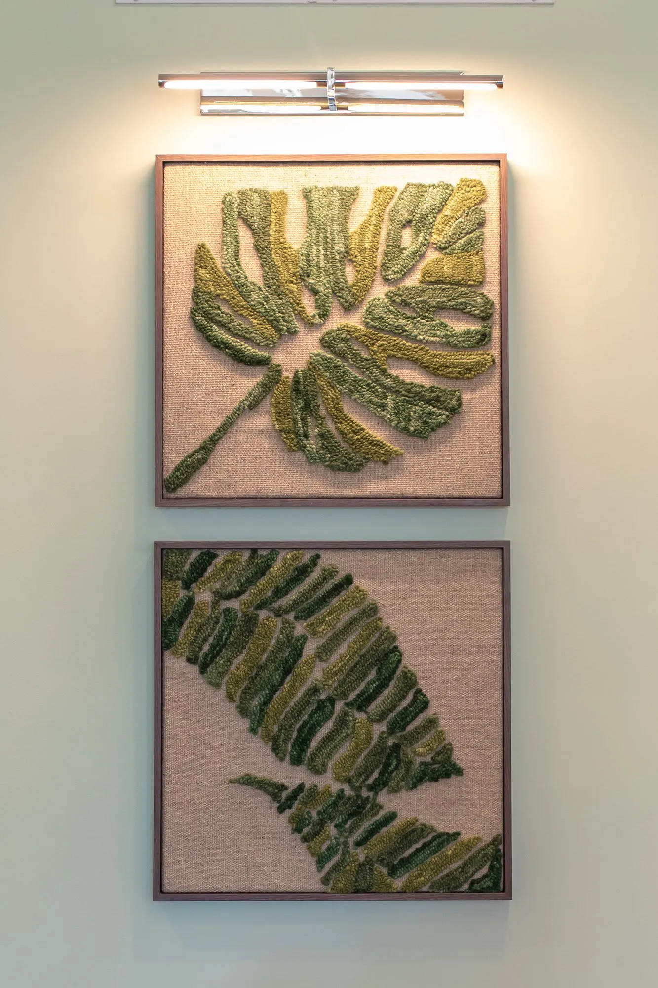 Multifamily interior detail: two framed textile artworks of green leaves lit by a picture light on a mint wall