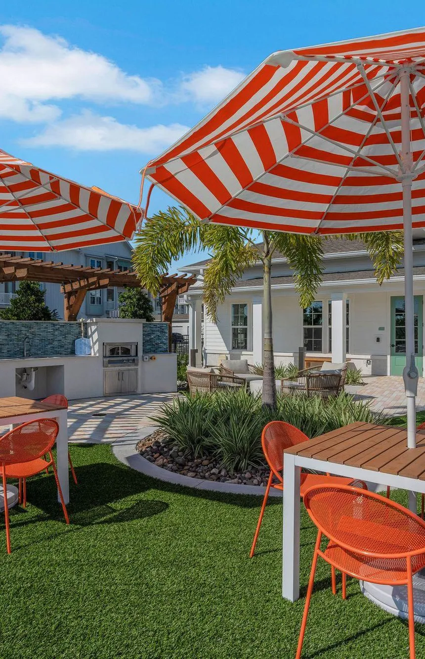 Multifamily amenity terrace with orange striped umbrellas, grills and lounge seating, interior design by Banko Design at The Brightly, Davenport, Florida