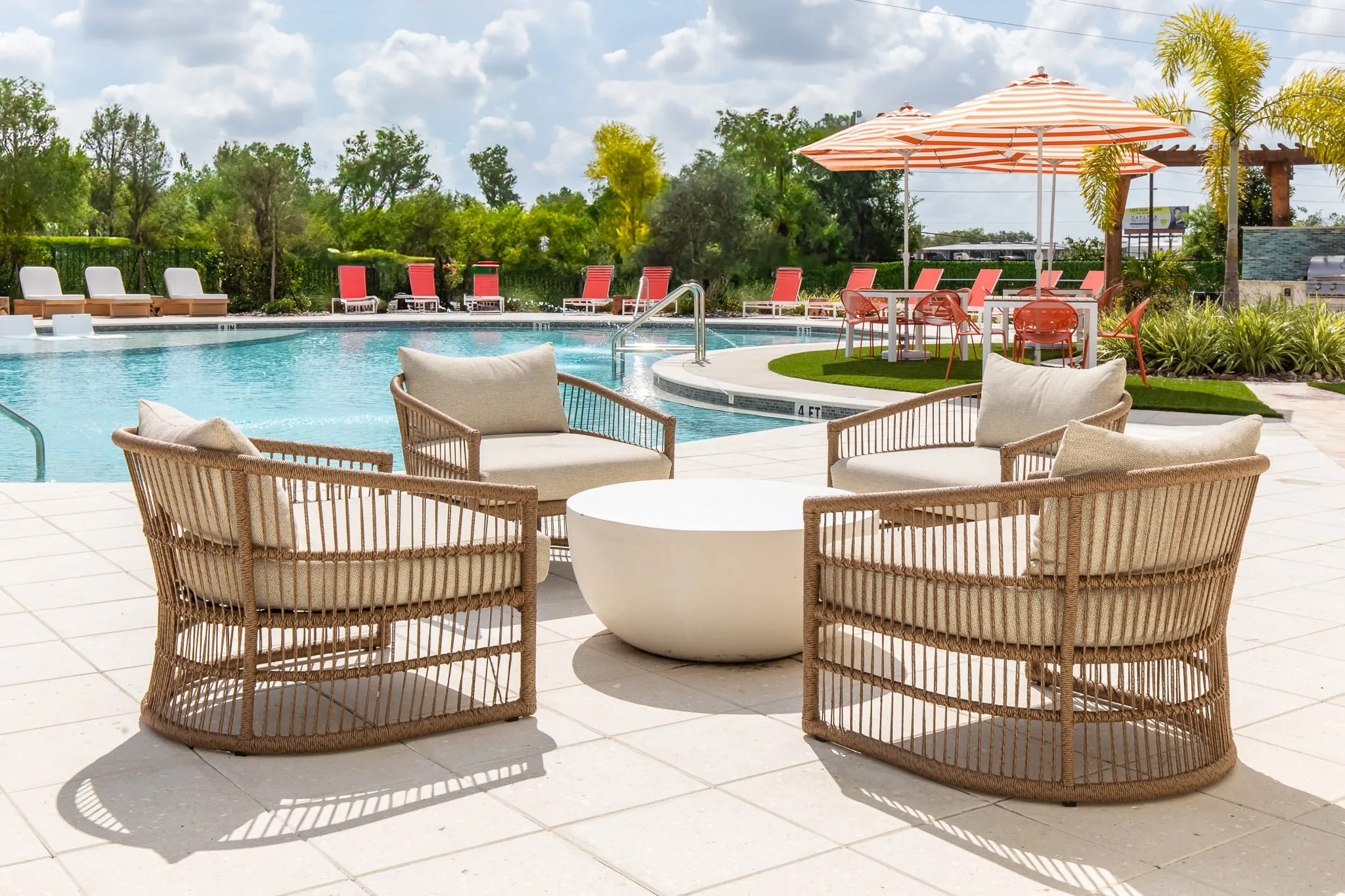 Multifamily amenity pool deck with woven rattan lounge chairs and orange and white striped umbrellas beside the water