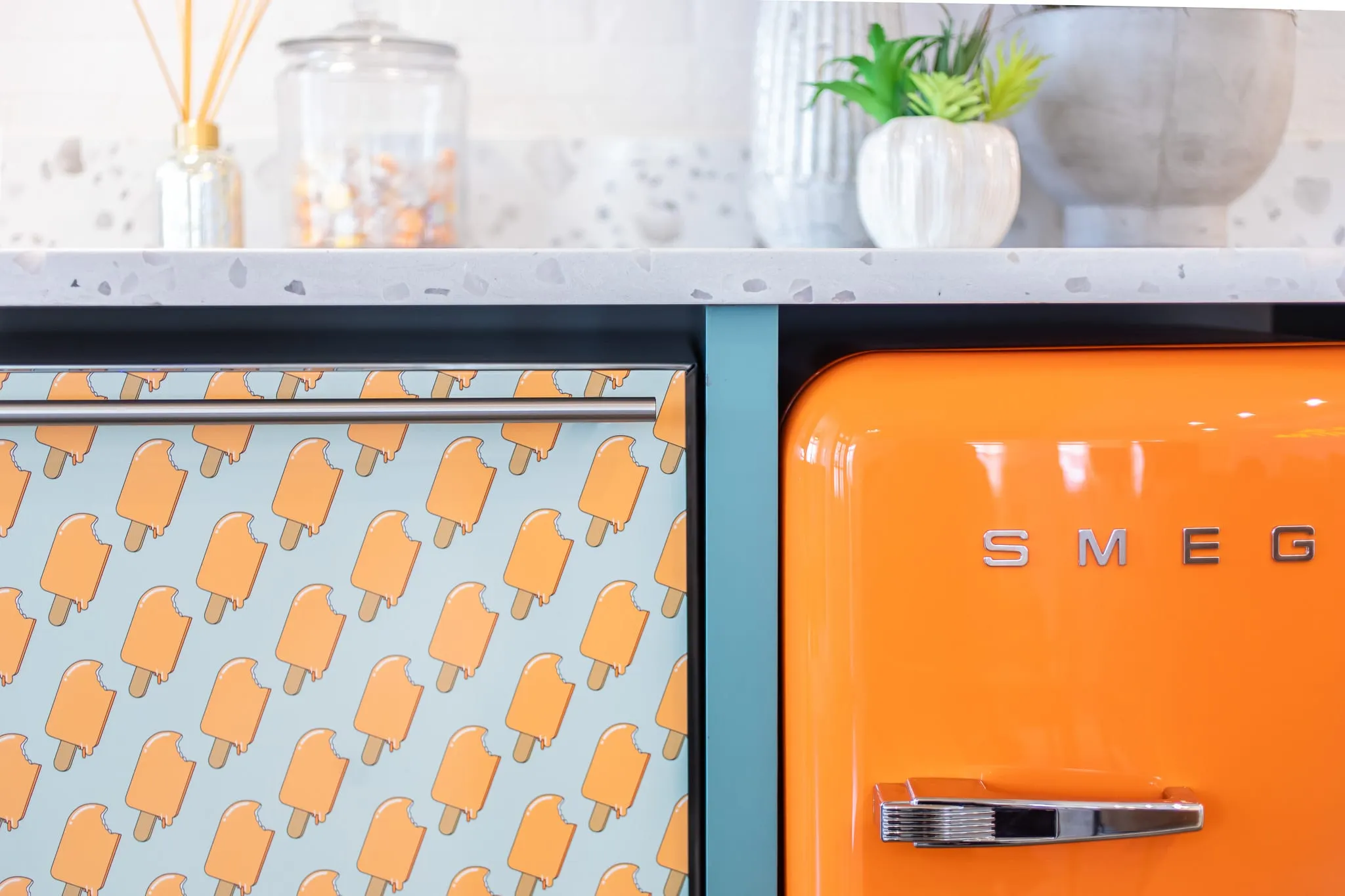 Multifamily interior detail: retro orange Smeg refrigerator against a popsicle-print panel on a terrazzo counter