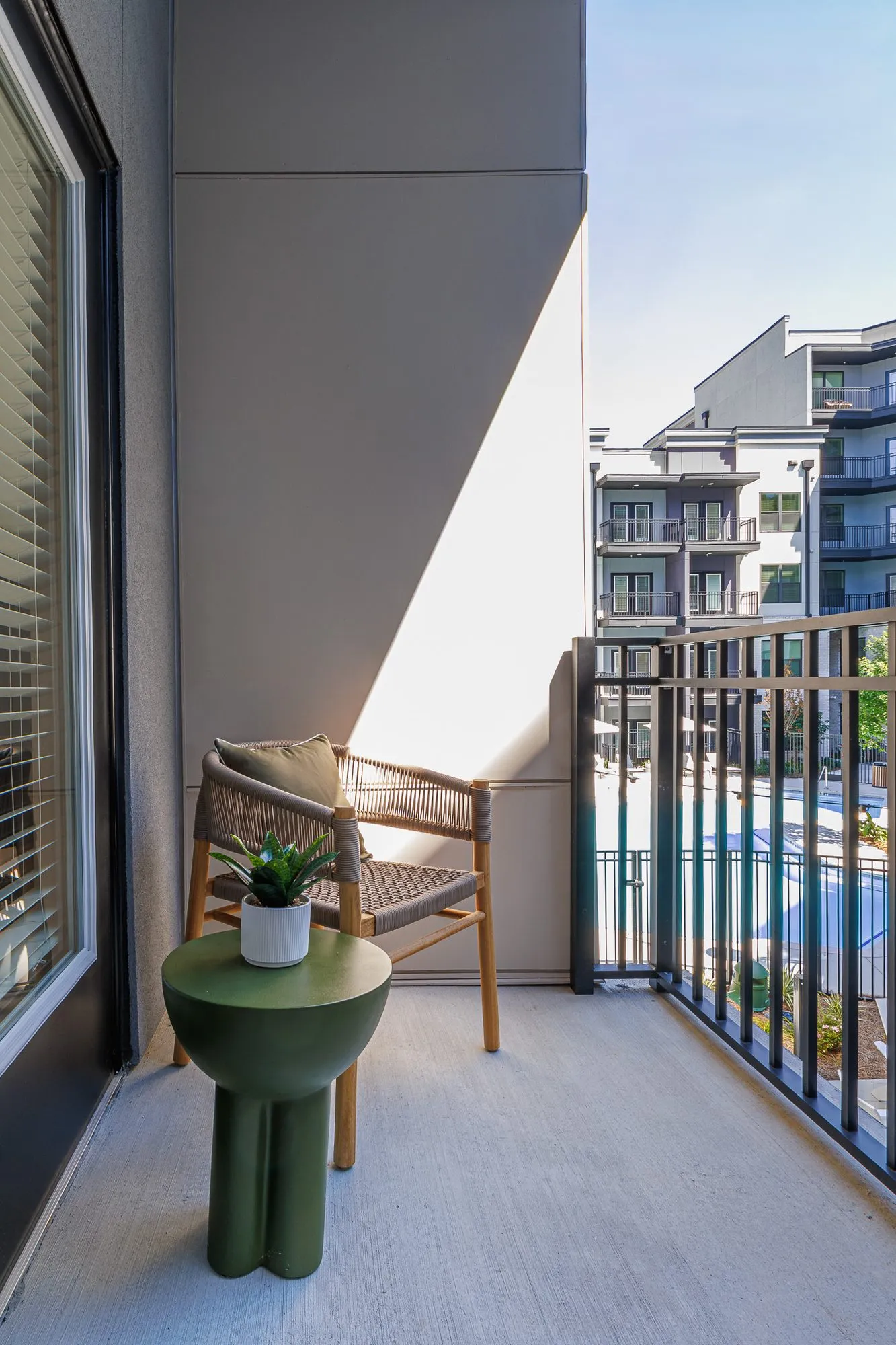 Multifamily apartment balcony with a woven chair and green side table, the pool and residential wings below