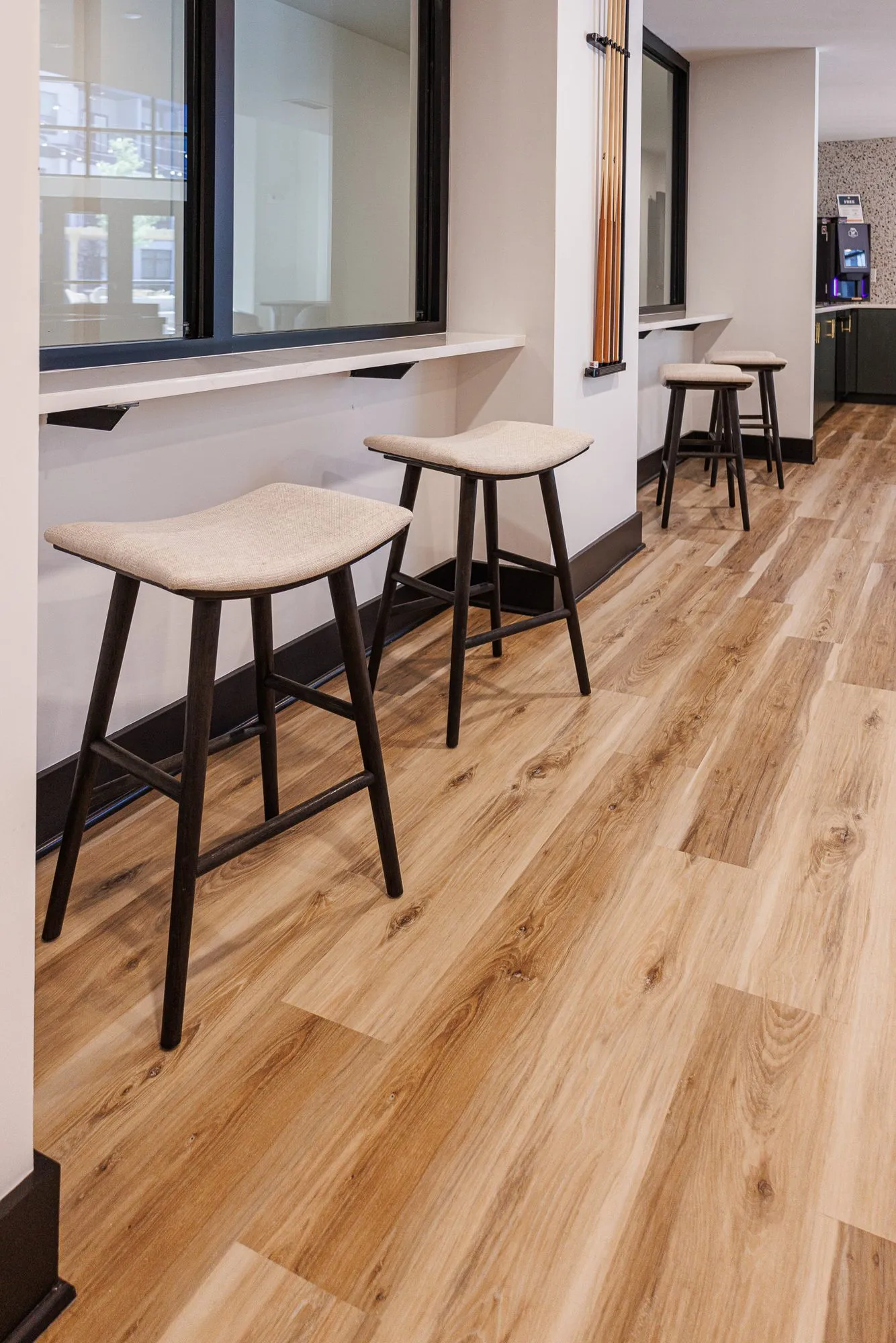 Multifamily interior detail: upholstered counter stools along a ledge below interior windows on a light wood plank floor