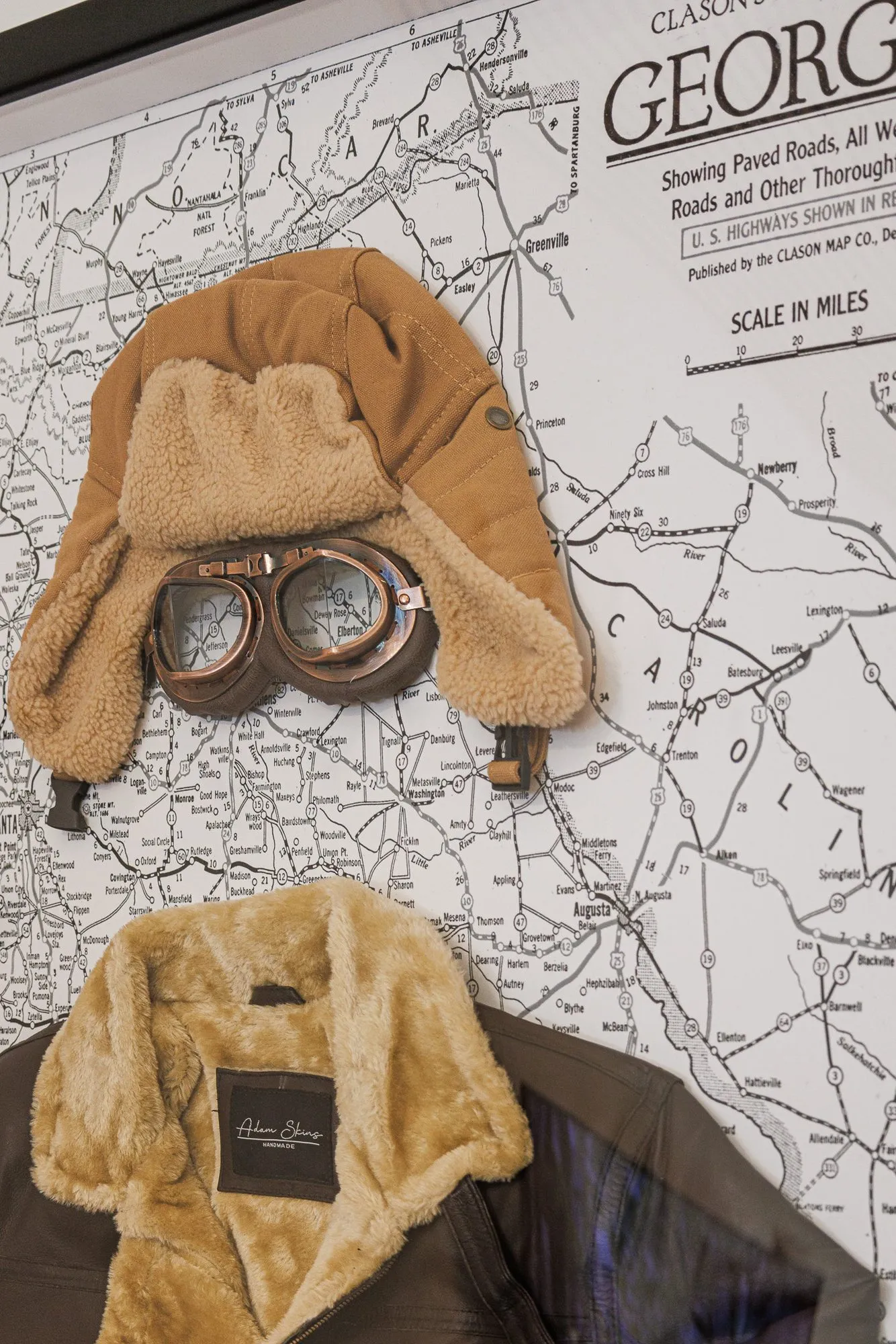 Multifamily interior detail: shearling aviator hat with goggles and a flight jacket mounted on a vintage road map