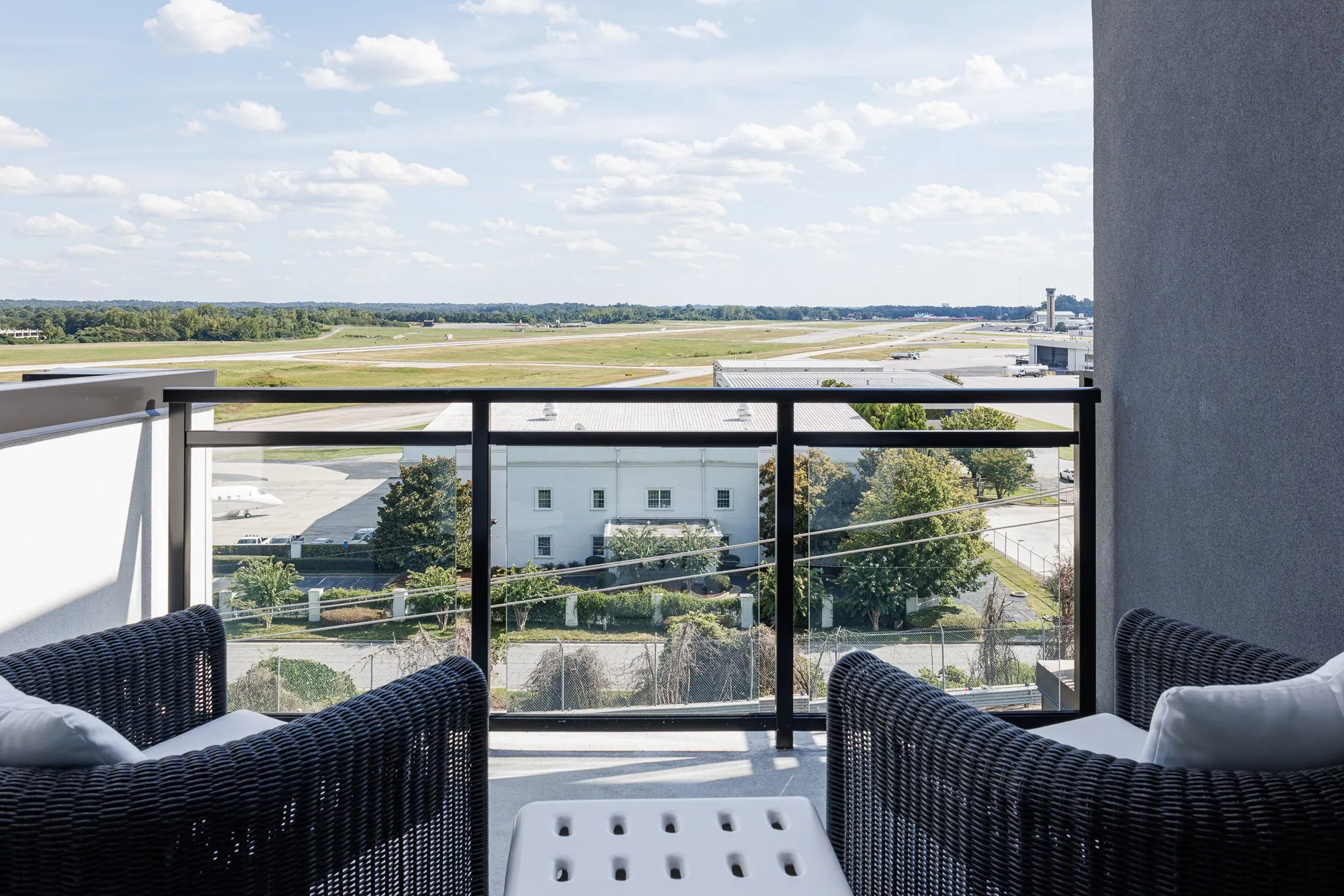 Multifamily apartment balcony with wicker lounge chairs and a white side table overlooking the airfield runway