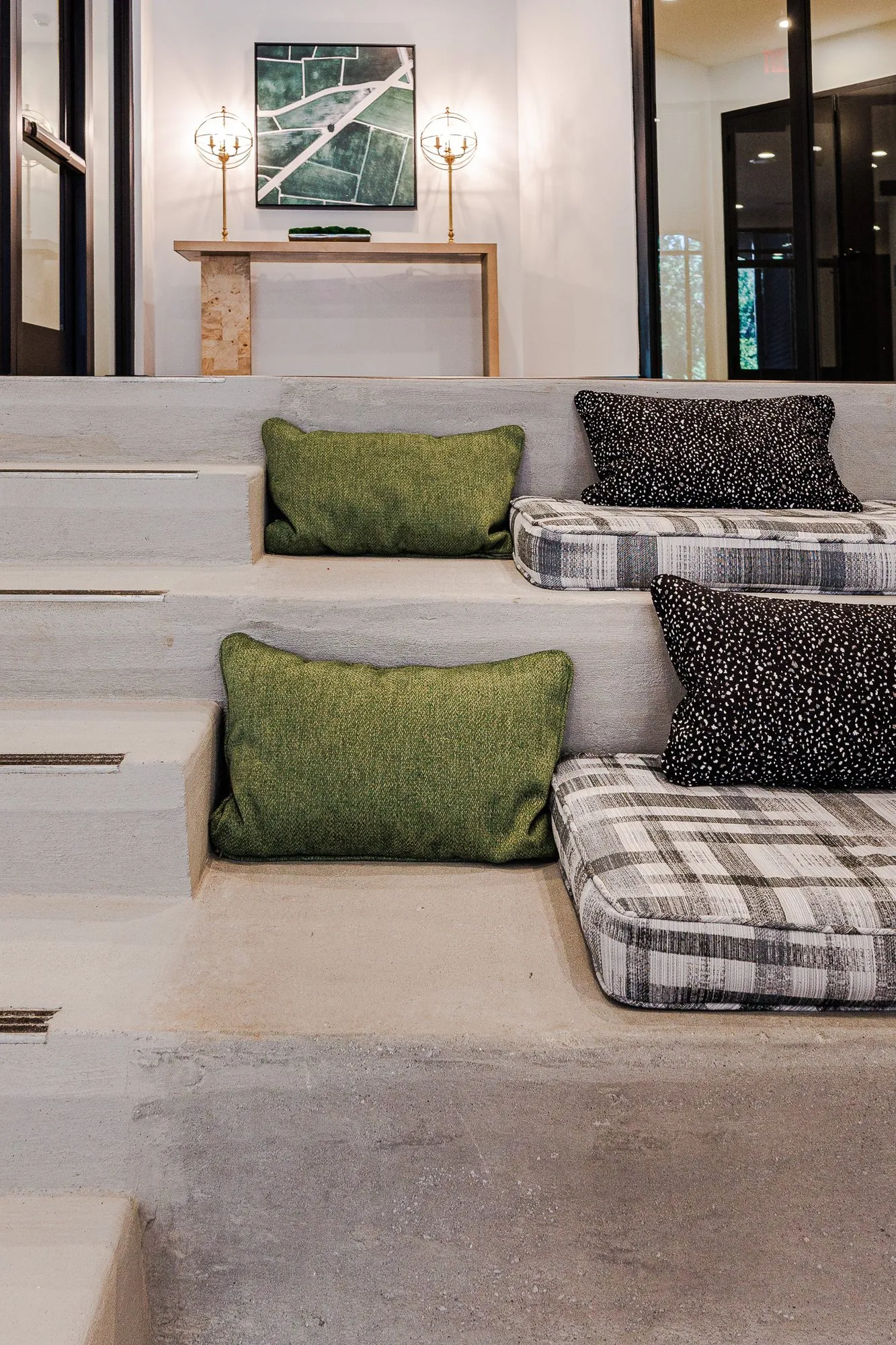 Multifamily amenity concrete bleacher steps with green, speckled and plaid cushions, a console with globe lamps above