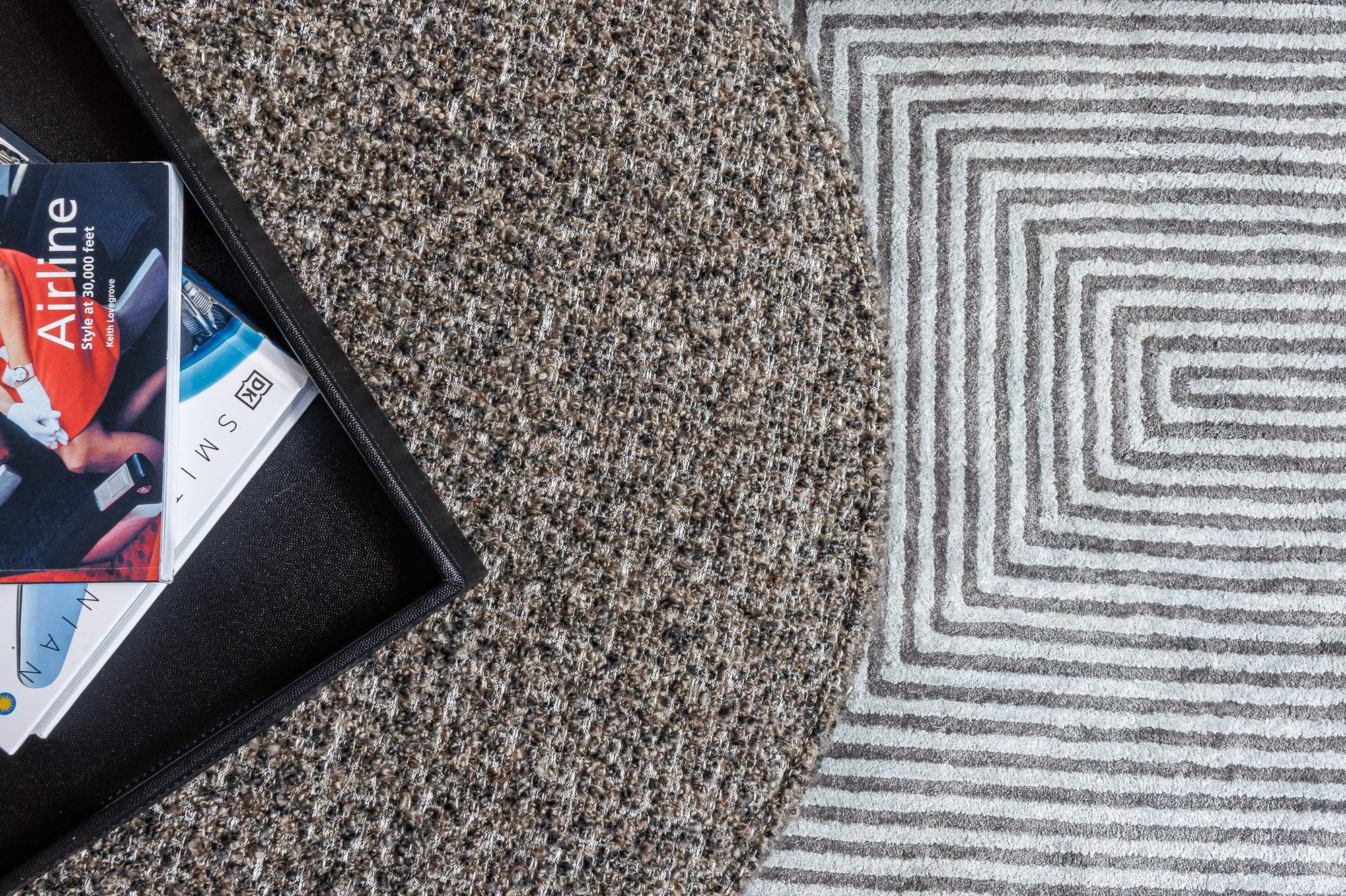 Multifamily interior detail: overhead view of a speckled round ottoman with a tray of magazines on a grey geometric rug
