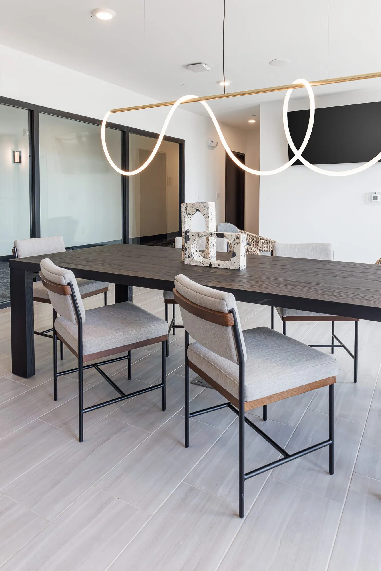 Multifamily interior detail: grey upholstered chairs at the dark dining table, rope light and wall screen above