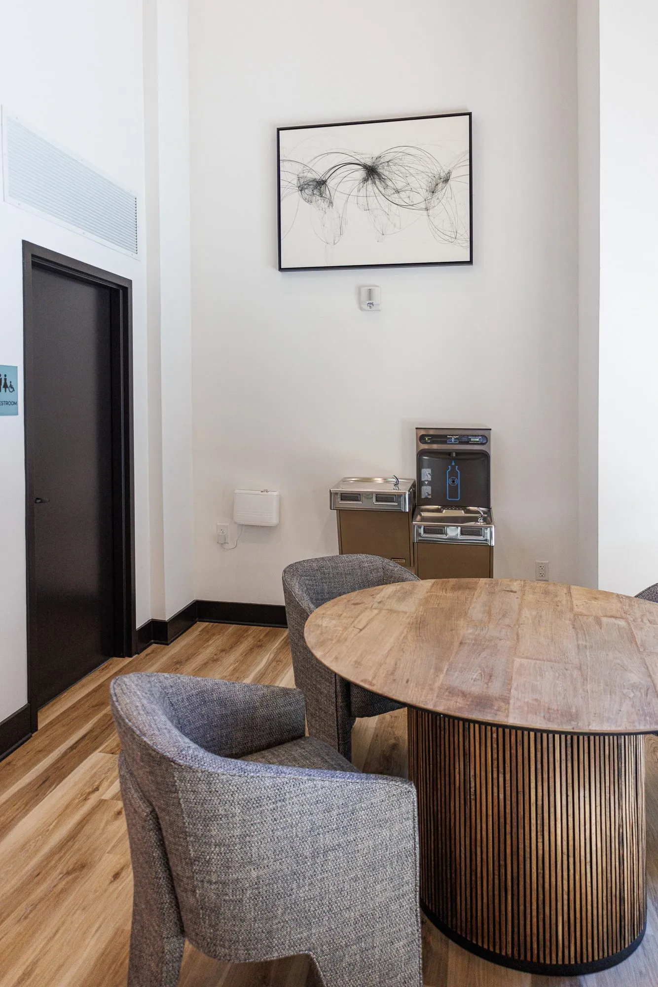 Multifamily interior detail: round wood table on a fluted base with grey boucle chairs, a water bottle filler and line art