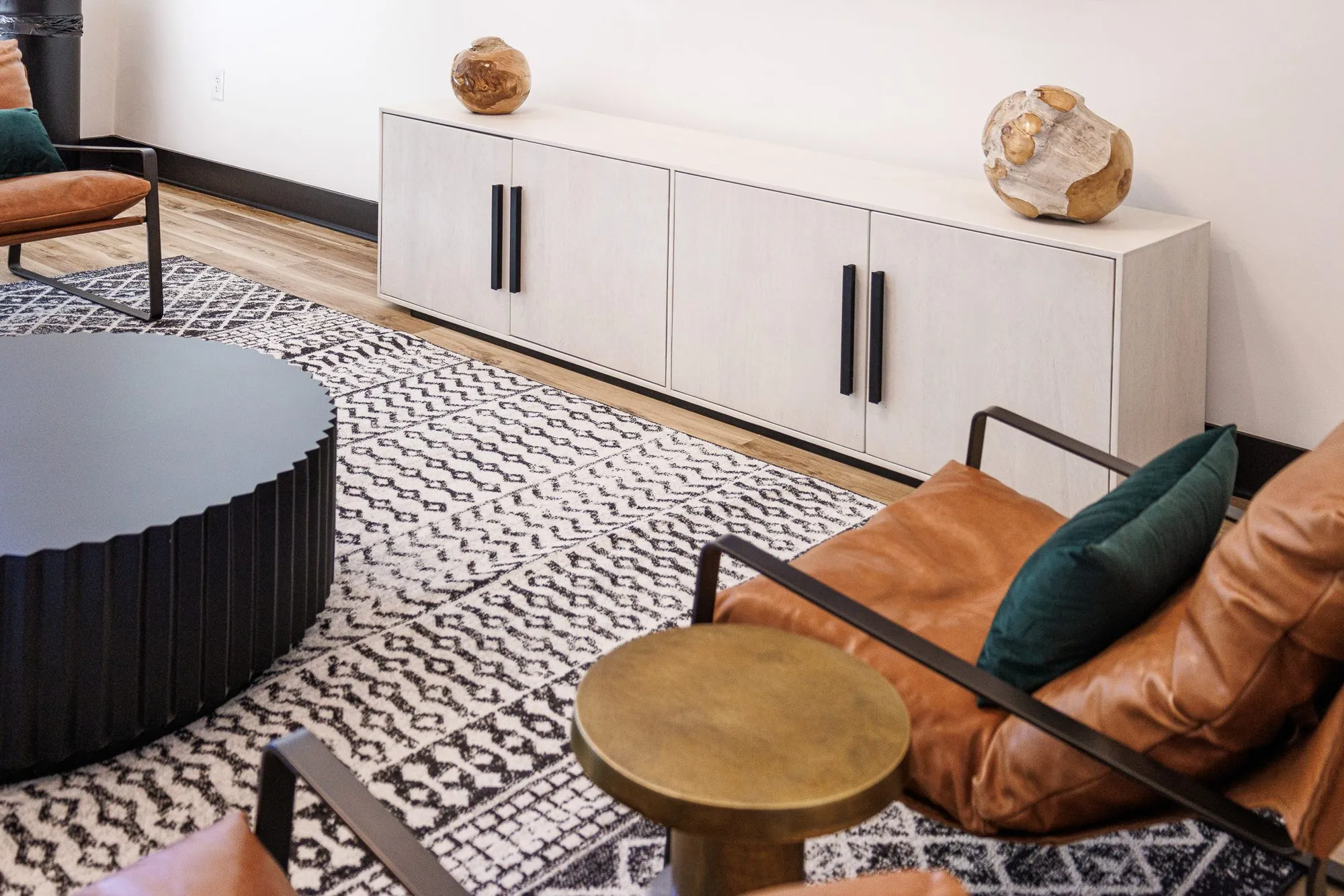Multifamily interior detail: cognac leather sling chairs with green pillows, a black fluted drum table and white credenza