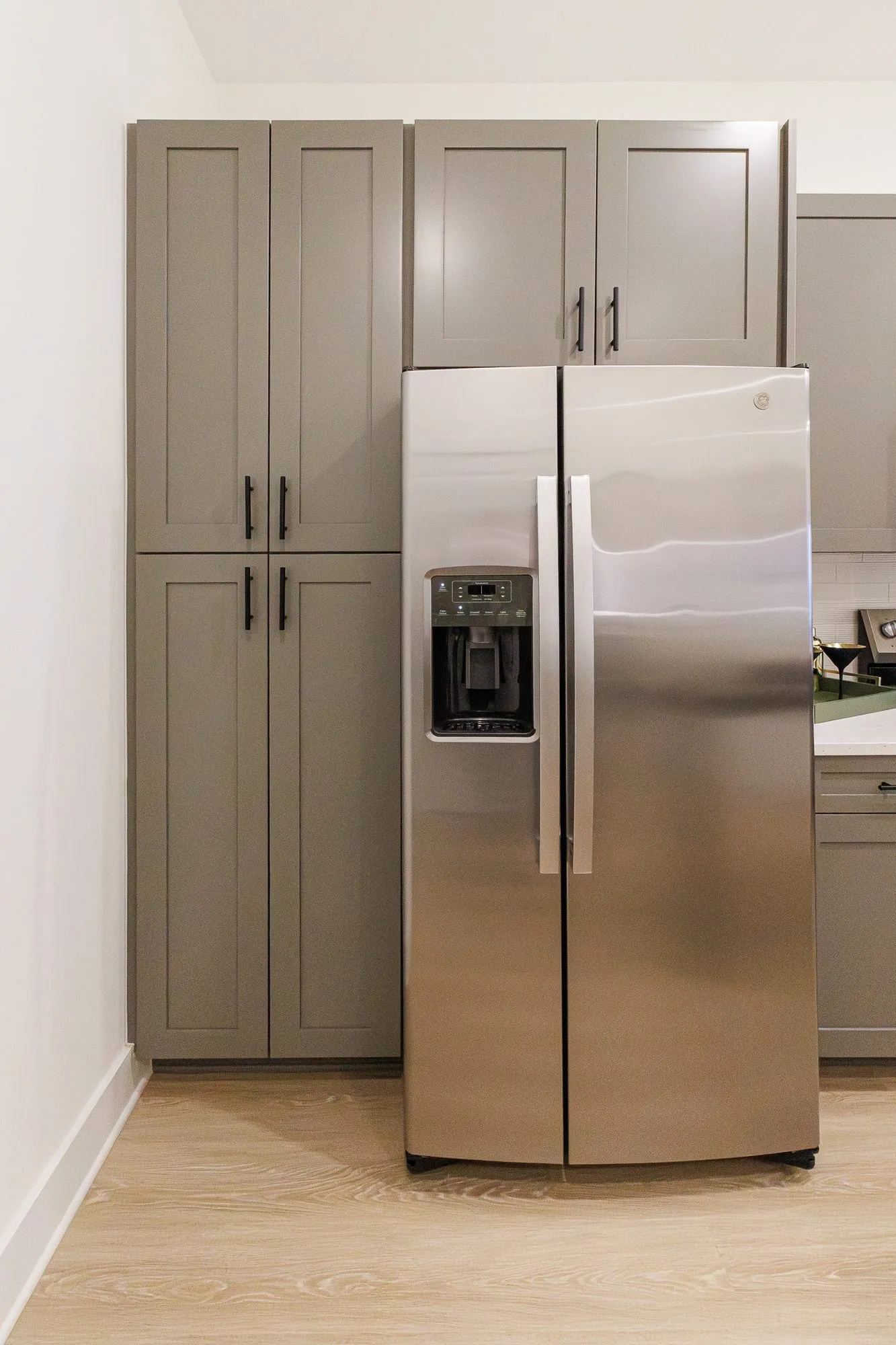 Multifamily model apartment kitchen with a stainless side-by-side refrigerator between grey shaker cabinets