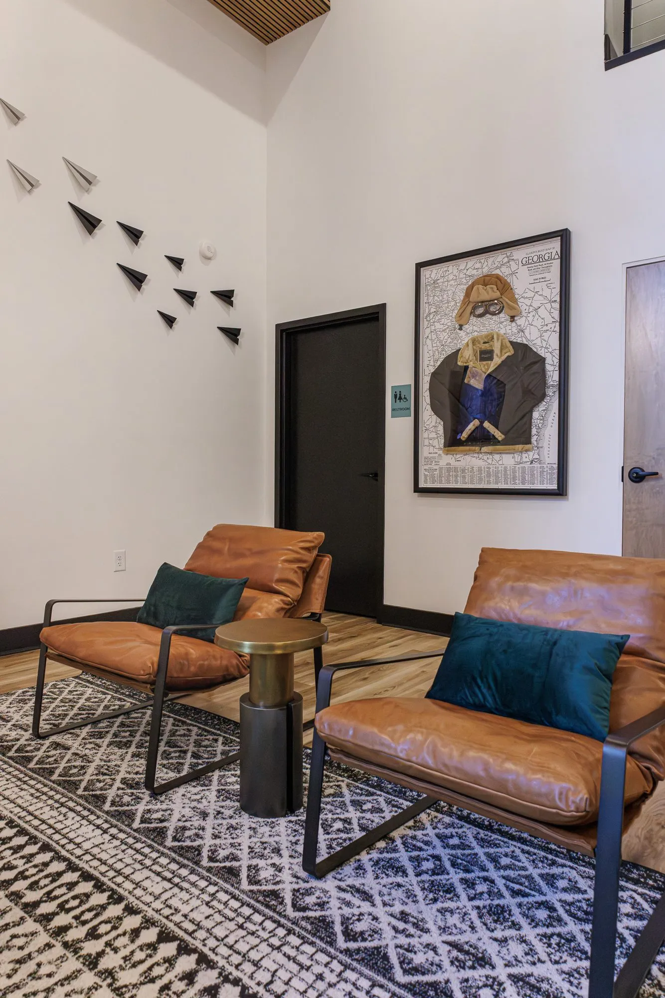 Multifamily interior detail: cognac leather sling chairs with teal pillows below folded paper planes and an aviator collage