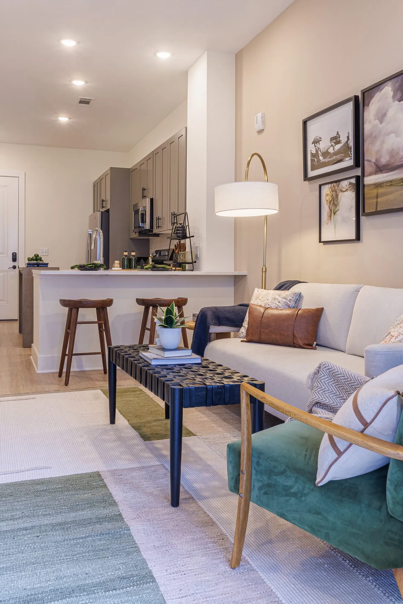 Multifamily model apartment living room with a cream sofa, green armchair and woven coffee table, kitchen beyond