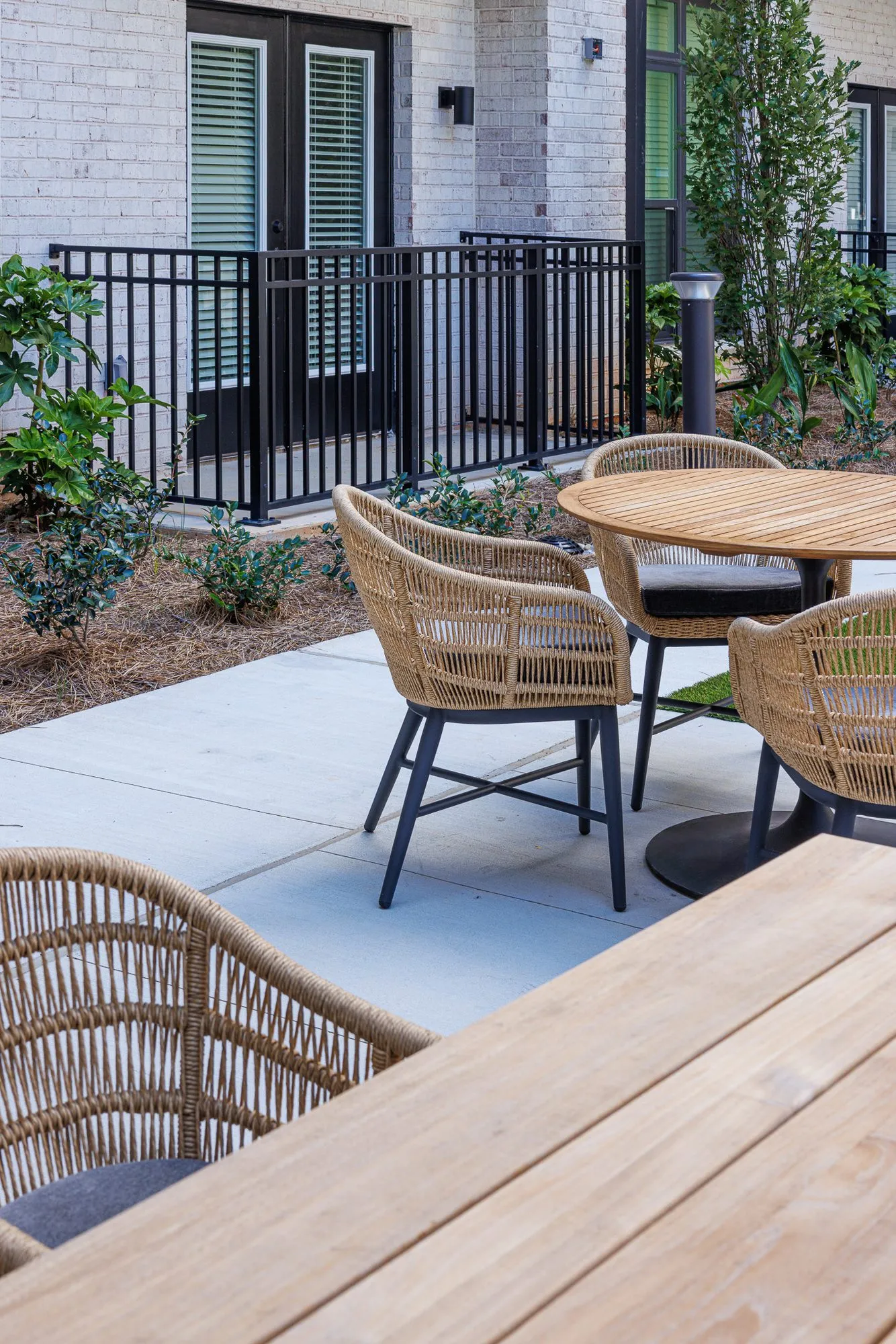 Multifamily amenity courtyard patio with woven dining chairs at round wood tables beside a black railing