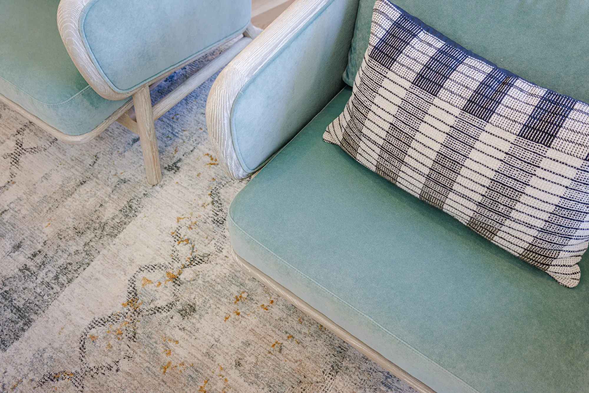 Multifamily interior detail: overhead view of mint velvet armchairs with a checked pillow on a pale patterned rug