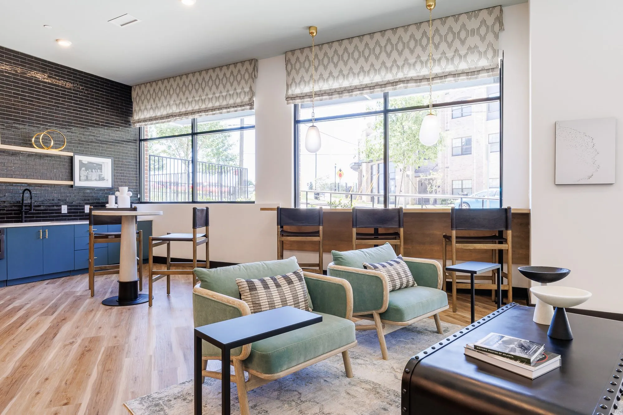 Multifamily amenity lounge with mint armchairs and counter chairs at the window, blue cabinetry and a black brick backsplash