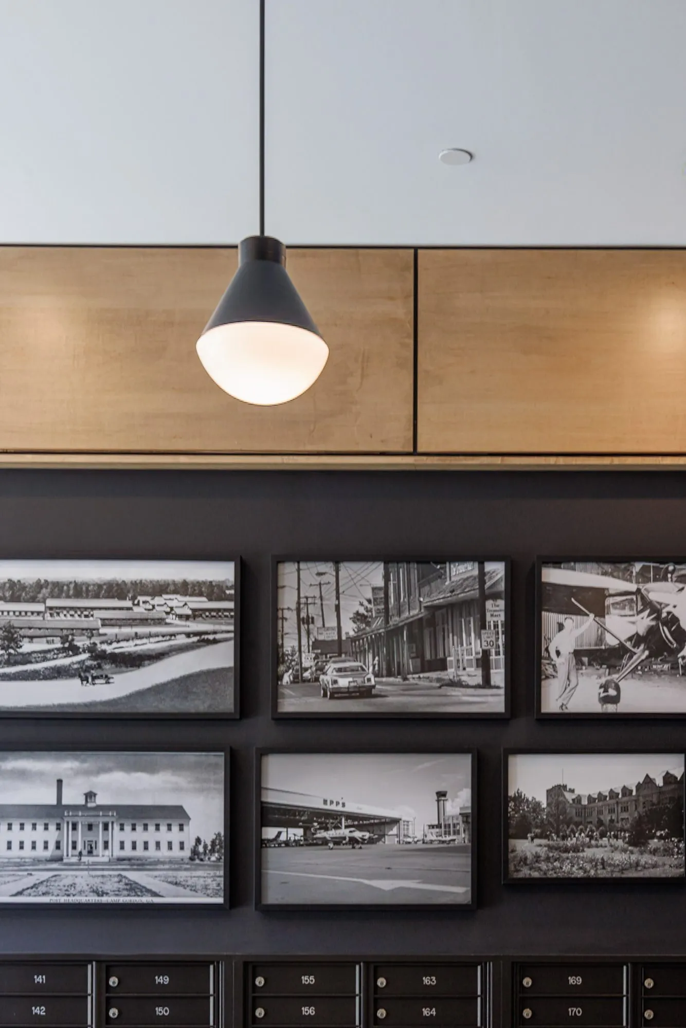 Multifamily interior detail: framed black and white historical photographs above the mailboxes, a black pendant overhead