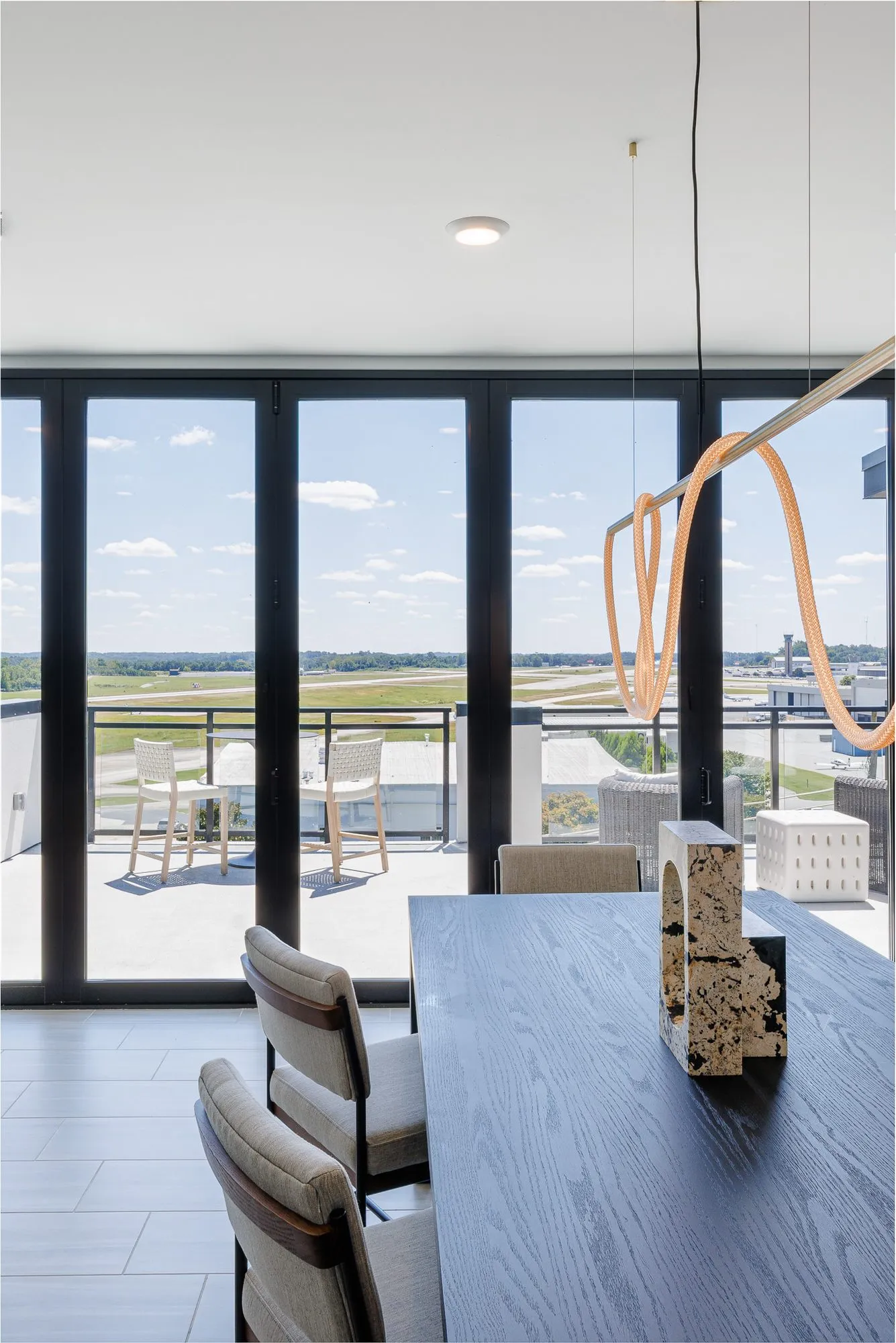 Multifamily amenity clubroom with folding glass doors to the terrace and airfield, a dark dining table and rope light