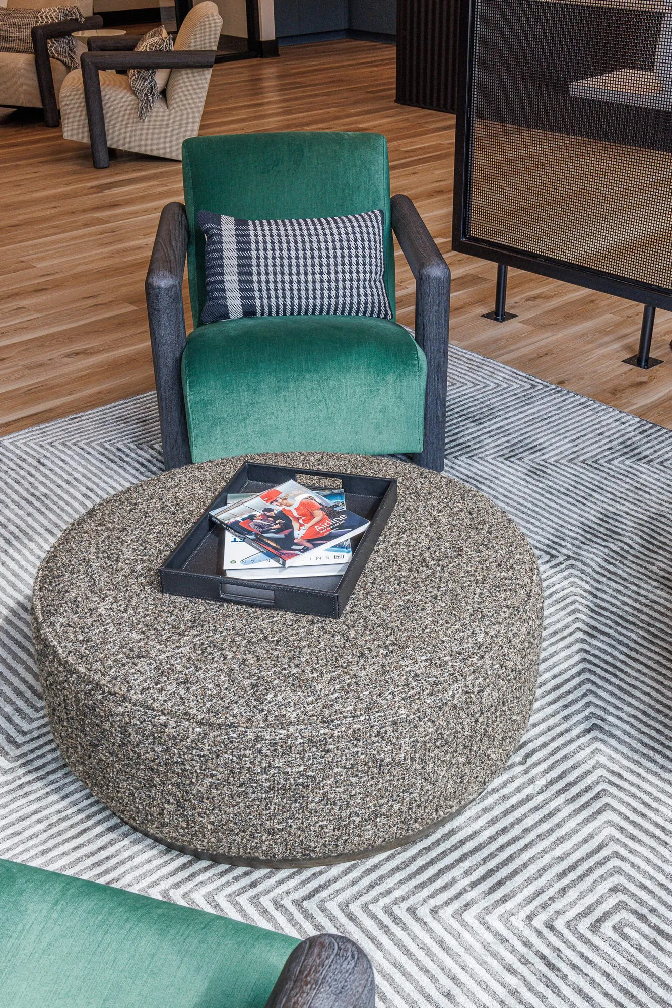 Multifamily interior detail: green velvet armchair with a houndstooth pillow behind a speckled ottoman with magazines