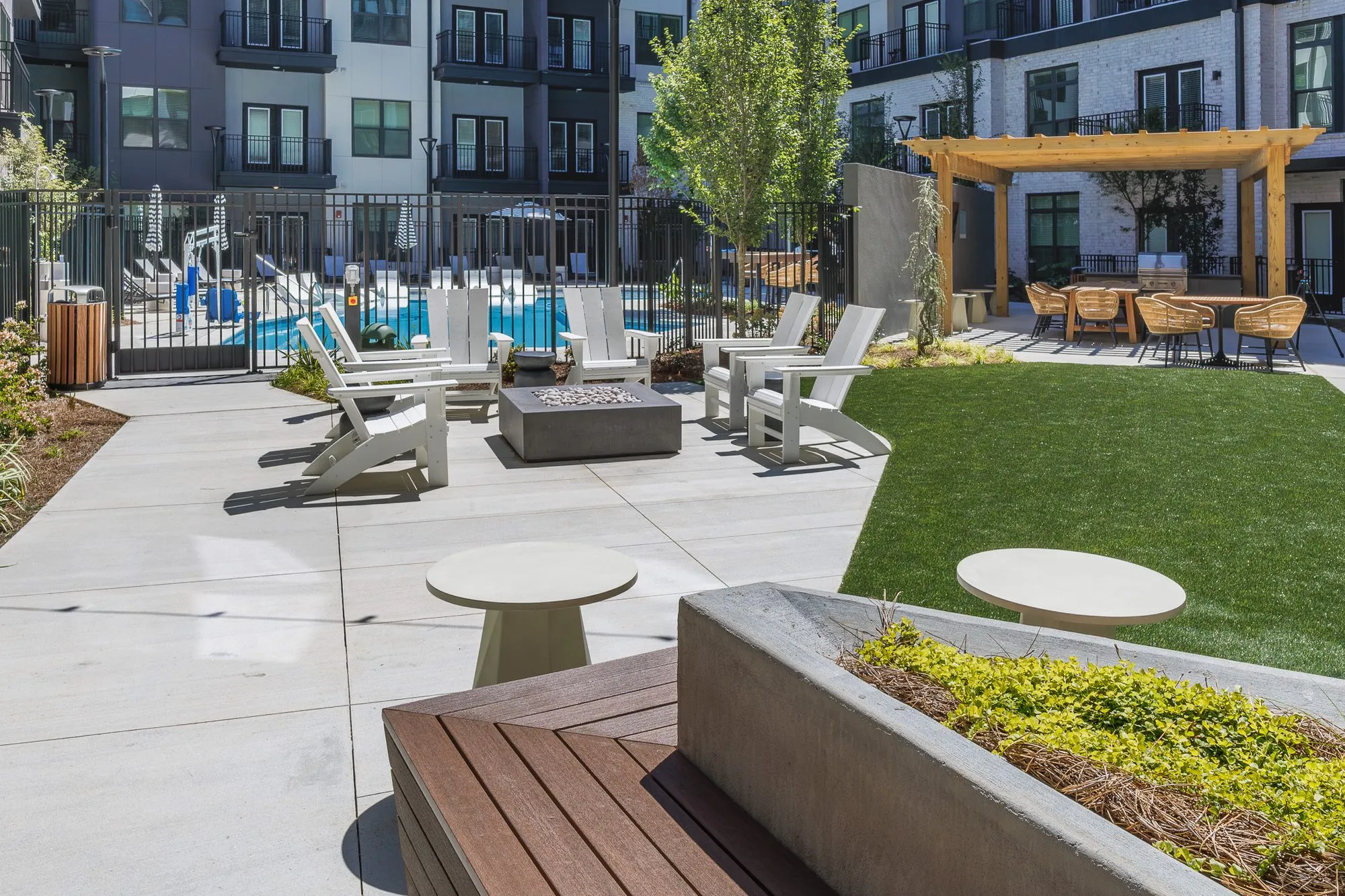 Multifamily amenity courtyard with wood bench seating and planters, Adirondack chairs, lawn, pergola and pool gate beyond