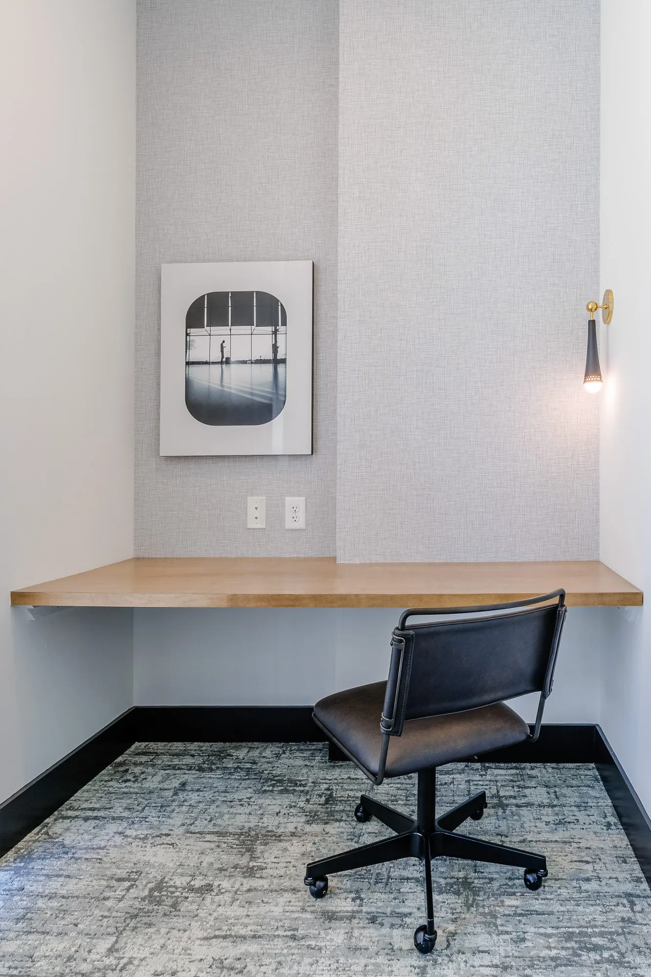 Multifamily work nook with a wood desk ledge, black leather task chair and a framed black and white photograph