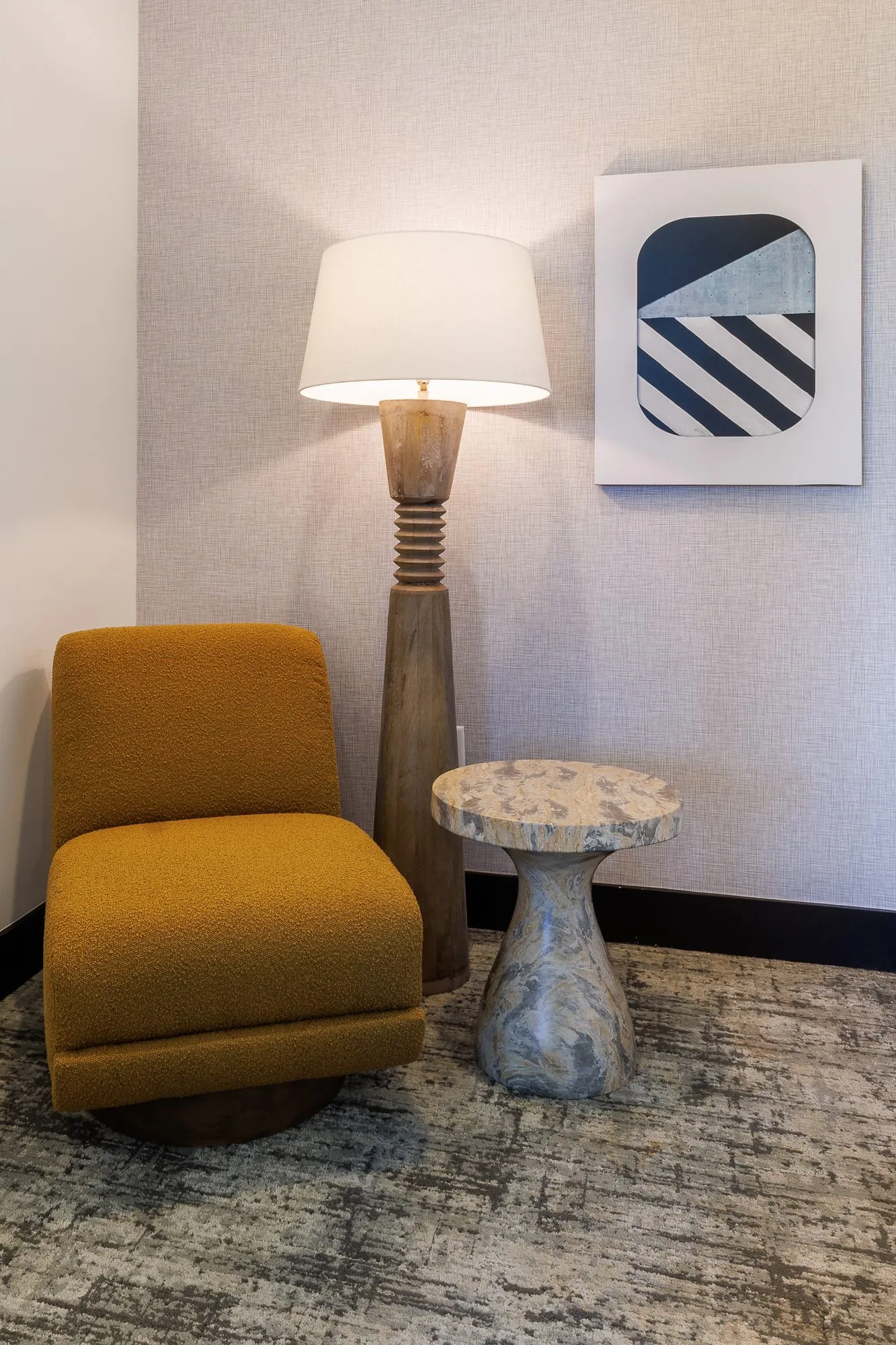 Multifamily interior detail: mustard swivel chair beside a turned wood floor lamp and stone side table, a striped print