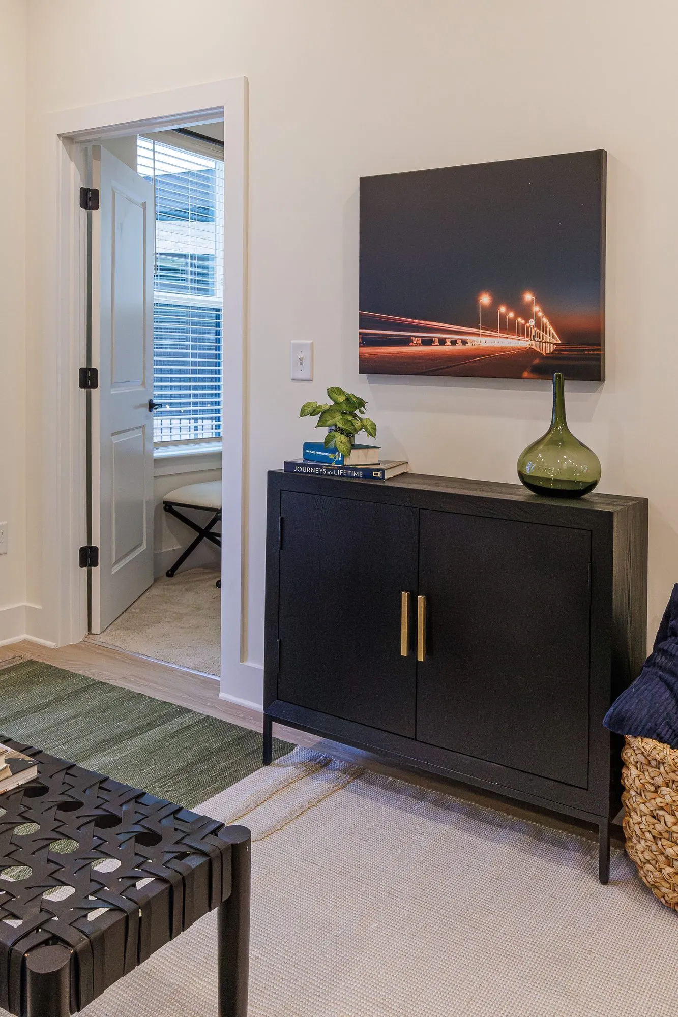Multifamily model apartment living area with a black cabinet, green glass vase and a night bridge photograph, bedroom door