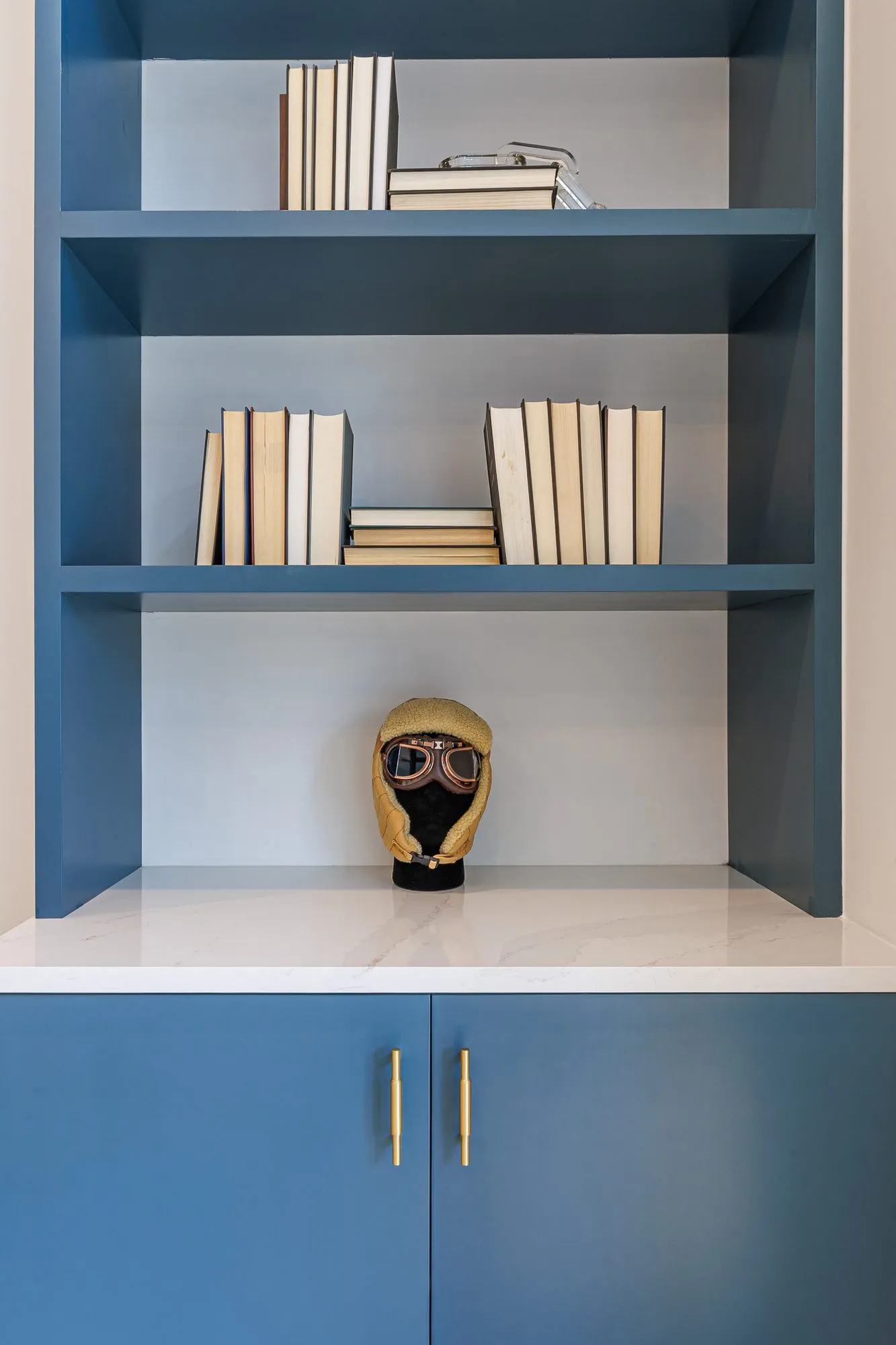 Multifamily interior detail: blue shelving with books and a sculpted head wearing an aviator cap and goggles