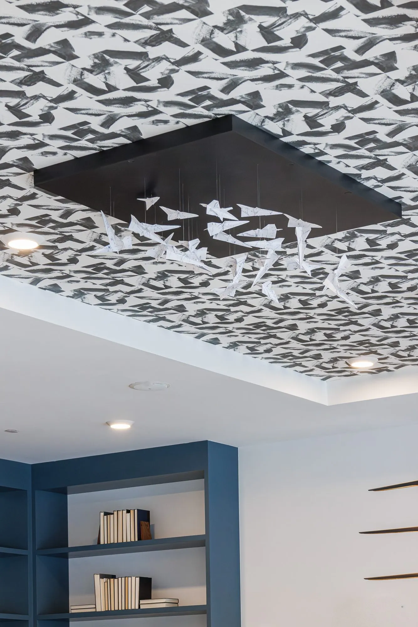 Multifamily interior detail: paper plane mobile hanging from a black panel on a patterned ceiling above blue shelving