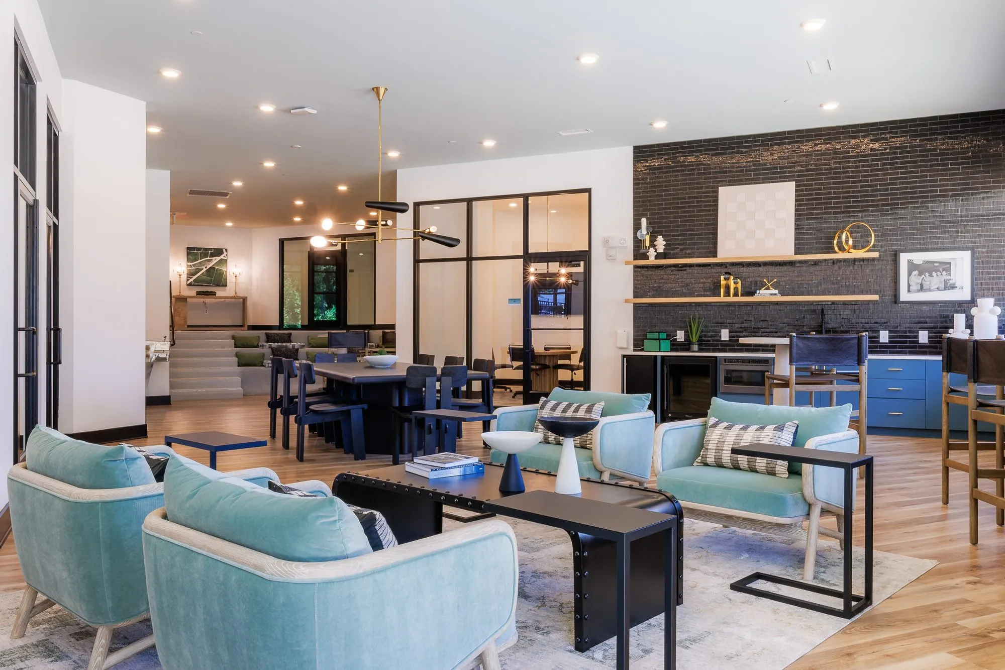 Multifamily amenity lounge with mint armchairs around a black coffee table, dining tables and the black brick coffee bar