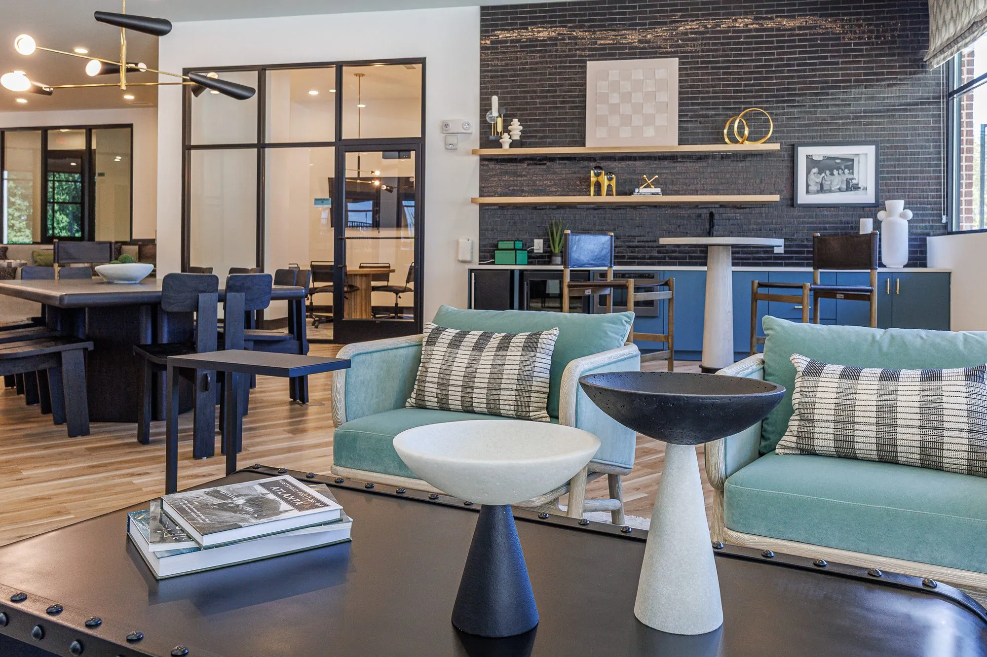 Multifamily interior detail: pedestal bowls on a black riveted coffee table before mint armchairs, black brick coffee wall