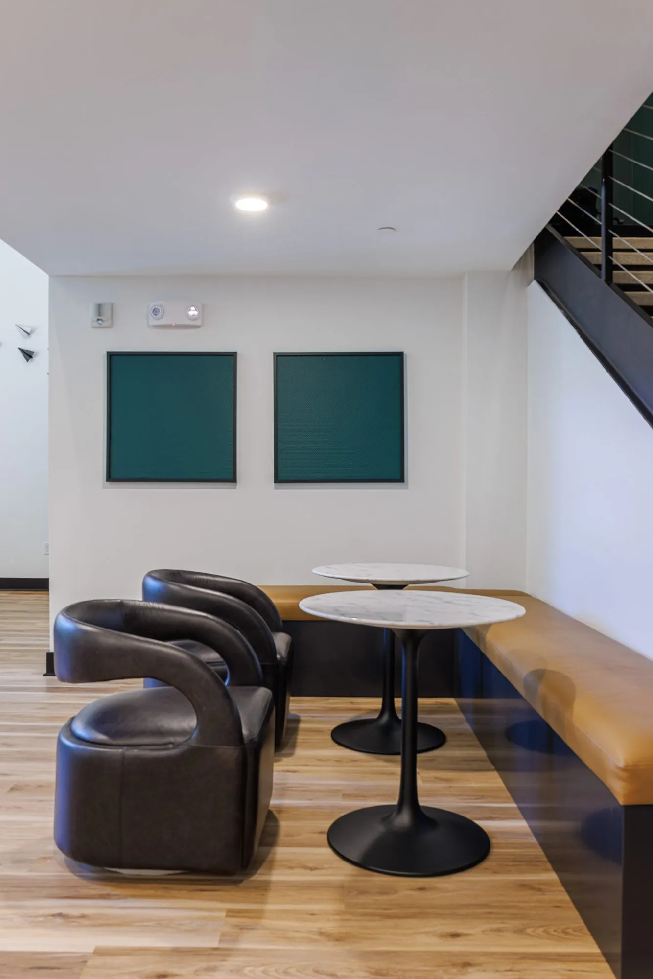 Multifamily amenity seating nook, black leather tub chairs and marble cafe tables at a leather banquette below the stair
