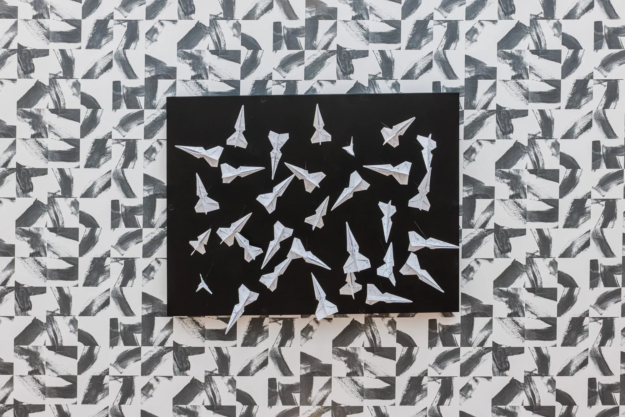 Multifamily interior detail: folded paper planes mounted on a black panel against black and white brushstroke wallpaper