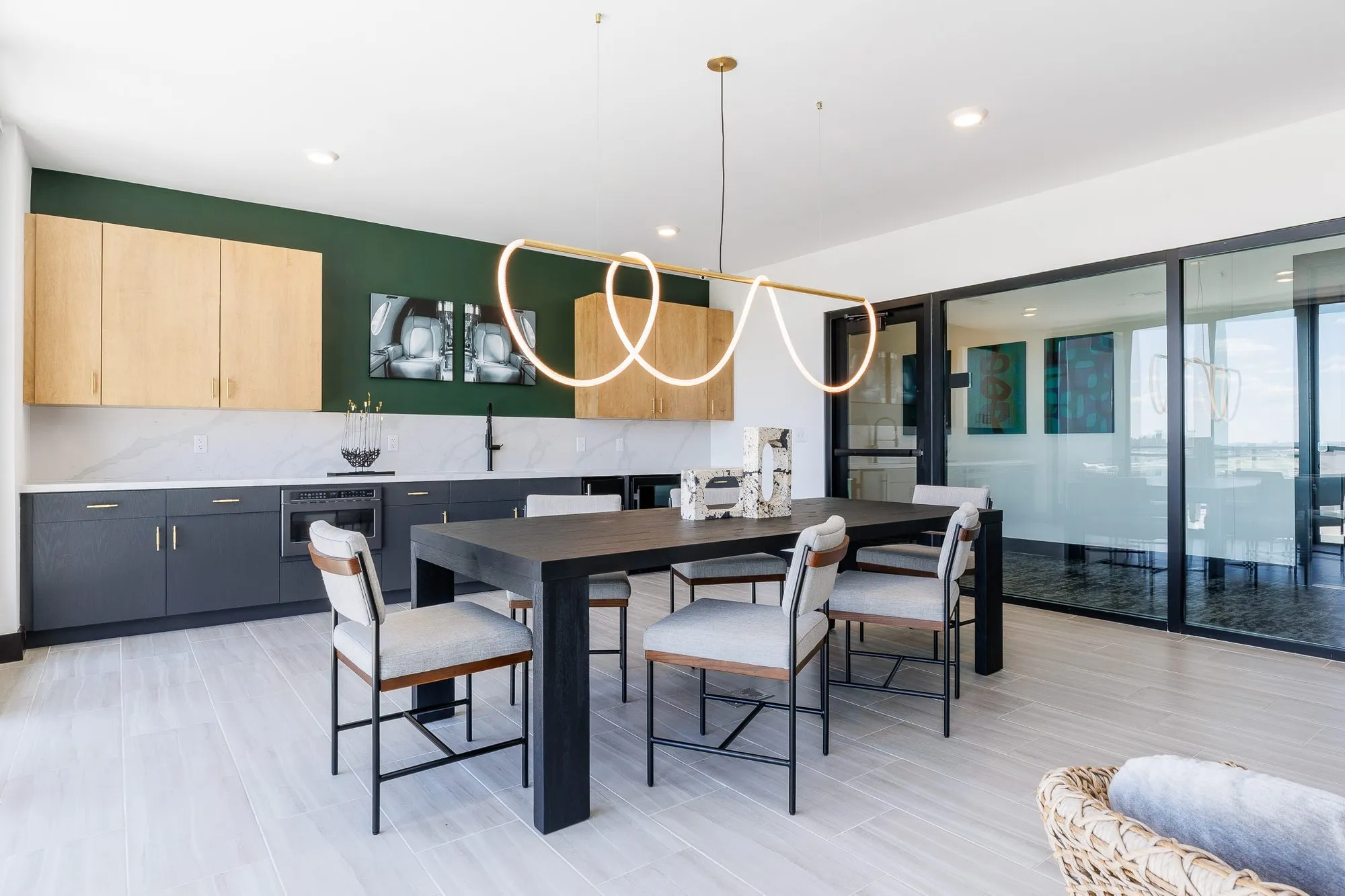 Multifamily amenity clubroom with a dining table and grey chairs under the rope light, a kitchenette and sliding doors behind