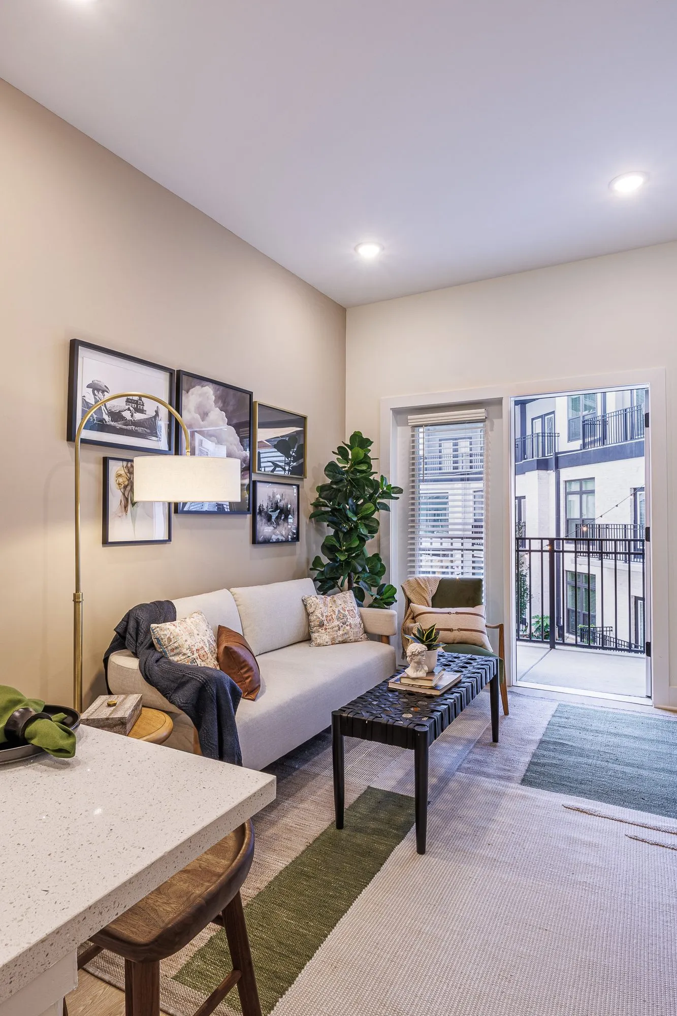 Multifamily model apartment living room with a cream sofa below a gallery wall, a fiddle leaf fig and a balcony door