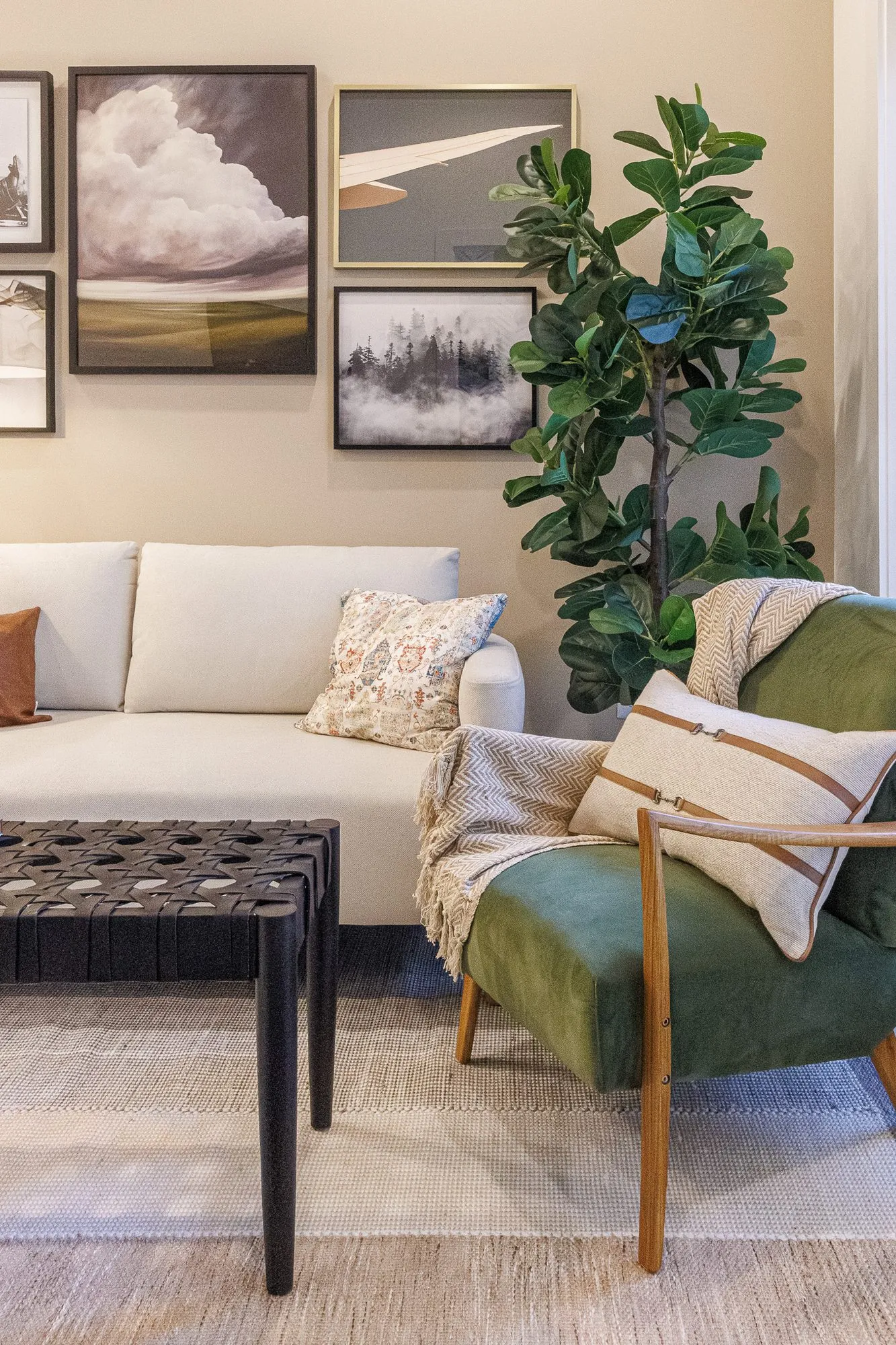 Multifamily interior detail: green velvet armchair and cream sofa below a gallery wall of framed photographs and a potted fig
