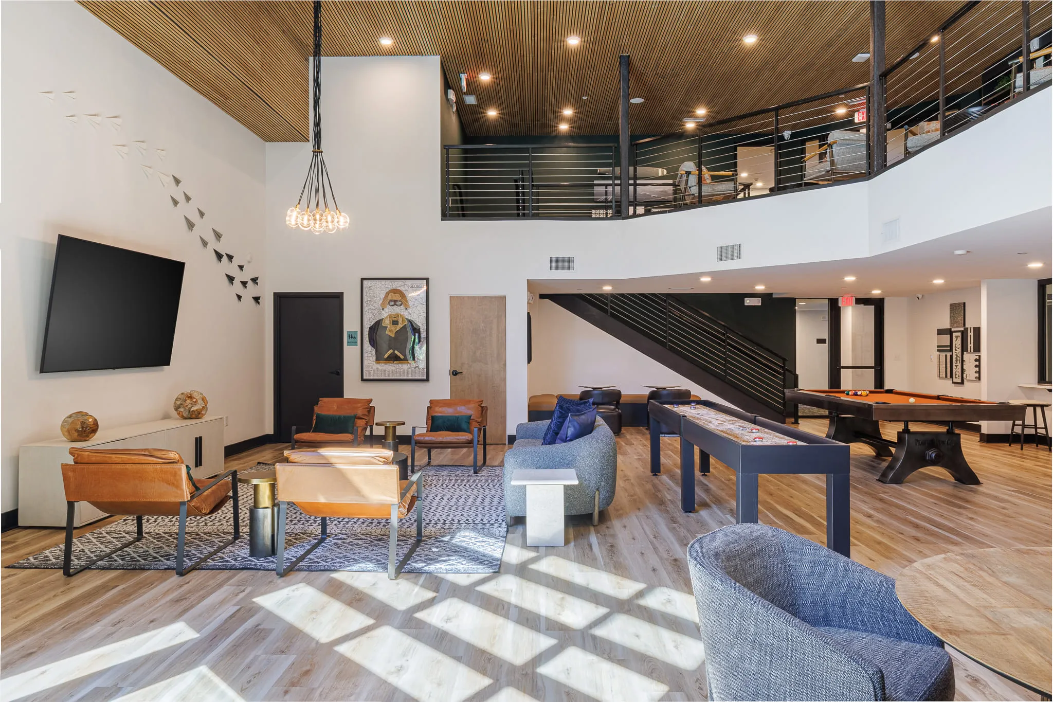 Multifamily amenity double-height clubroom with leather sling chairs, shuffleboard and pool table below the mezzanine