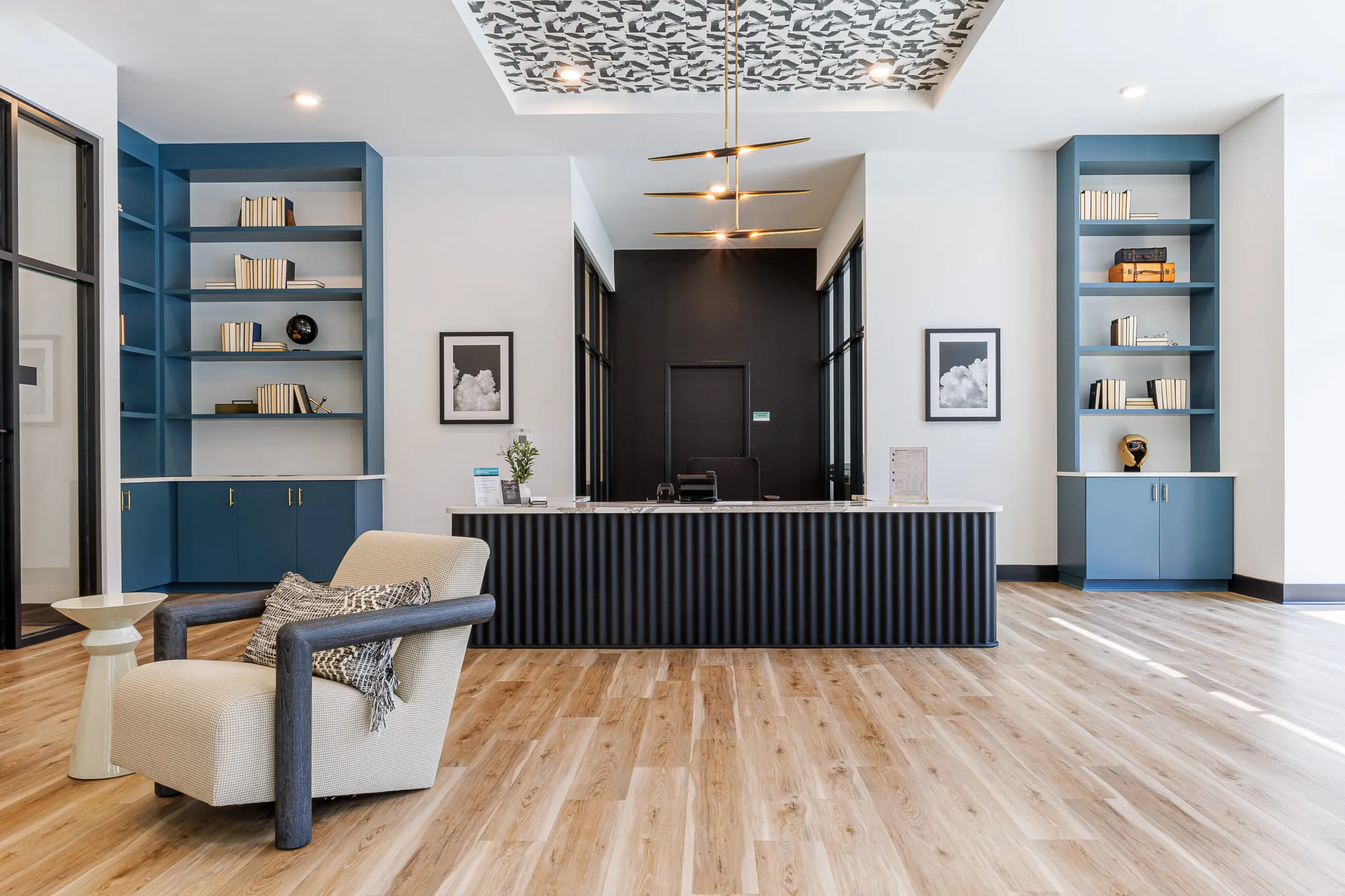 Multifamily amenity leasing office with blue built-in shelving flanking a fluted reception desk under a patterned ceiling