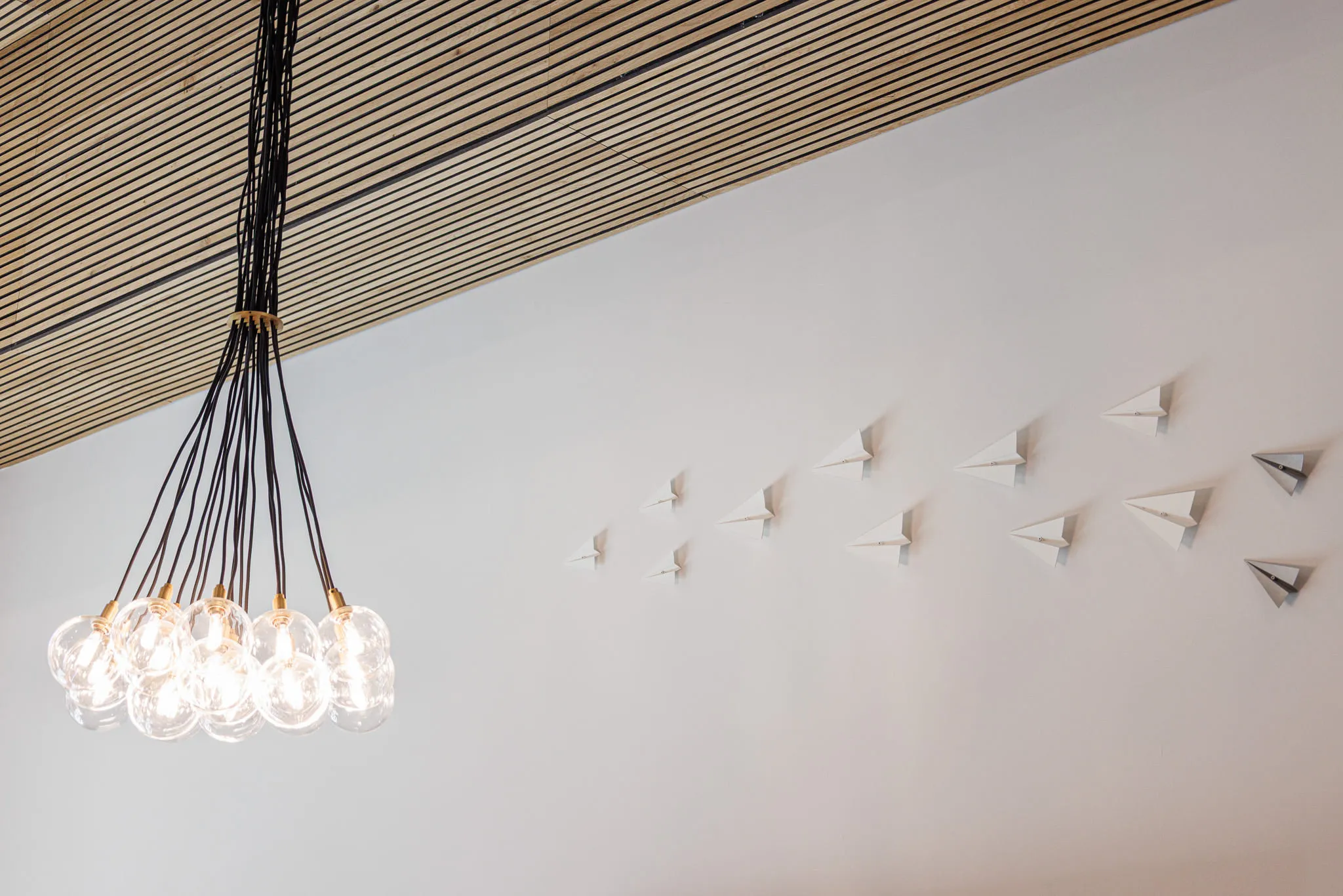 Multifamily amenity paper airplane installation: folded planes climbing the wall beside a cluster of glass globe pendants