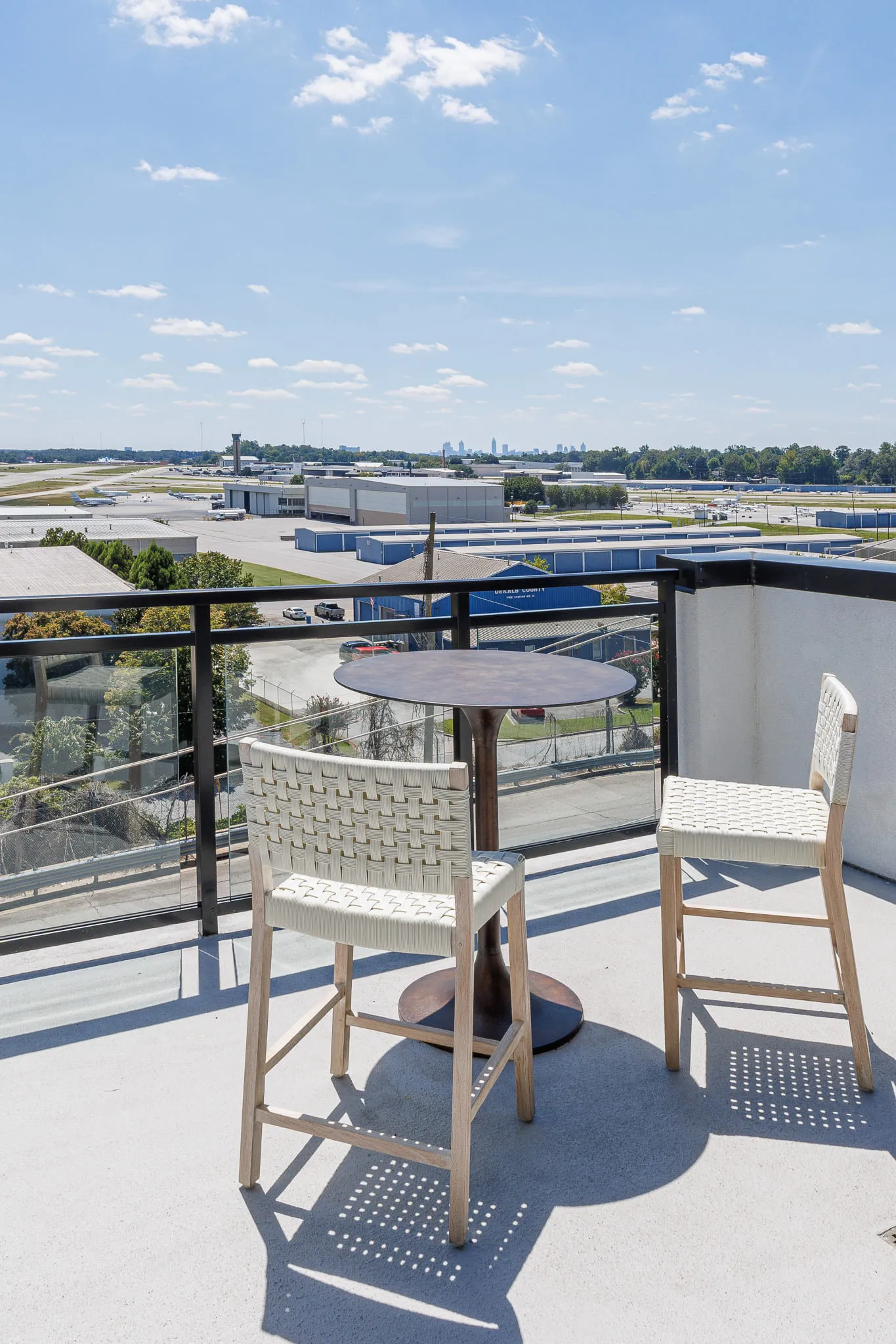 Multifamily amenity rooftop deck with woven chairs and a bistro table at the rail overlooking the PDK runway