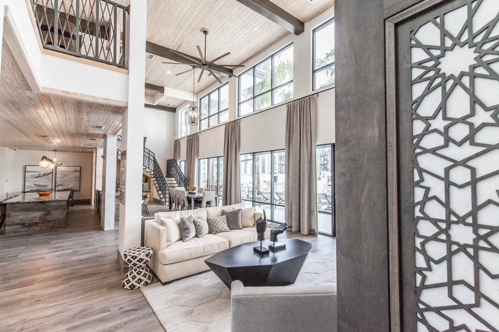 Multifamily amenity clubroom lounge with a cream sofa and dark coffee table by tall windows and a pierced metal screen