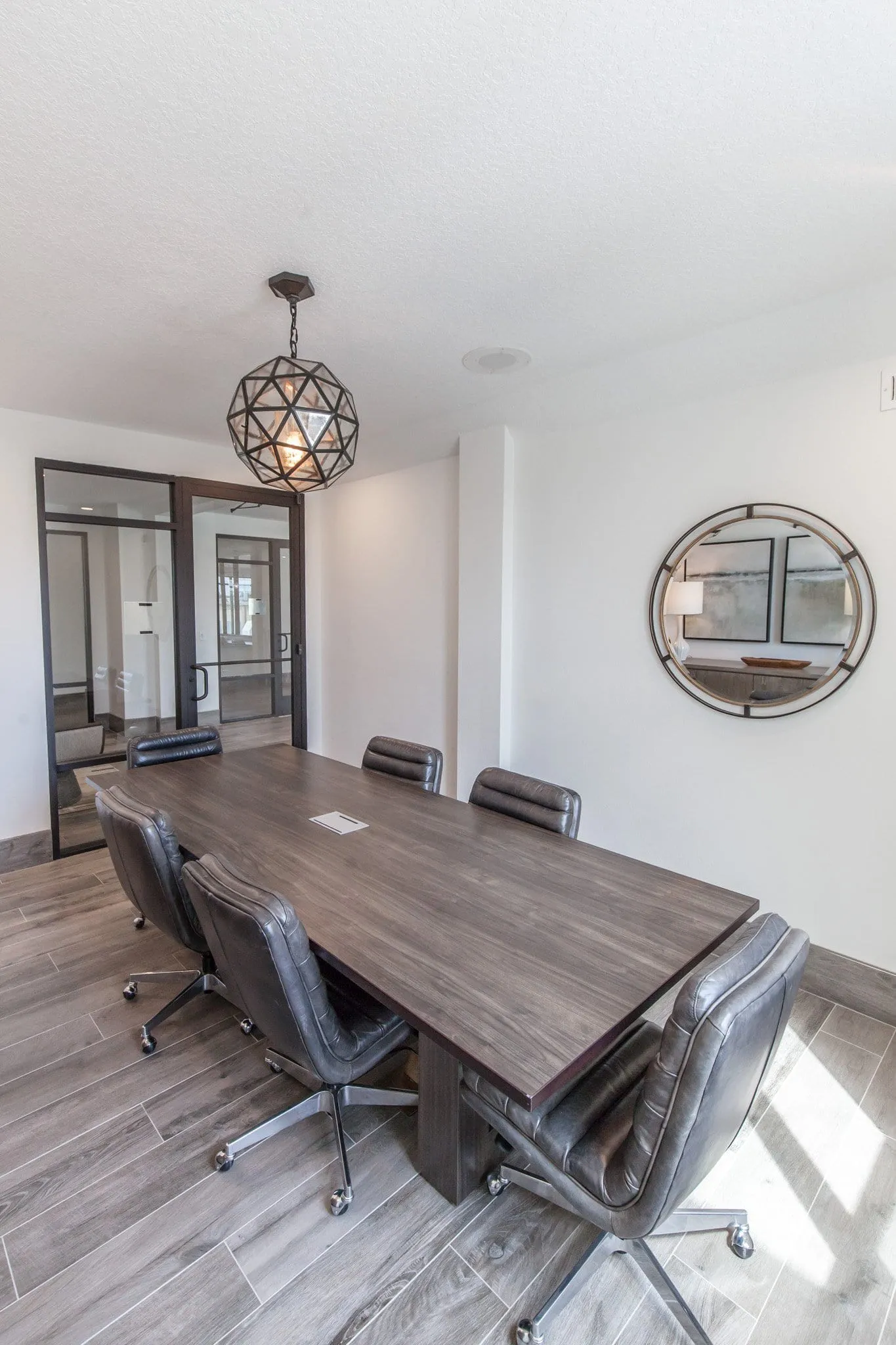 Multifamily amenity conference room with a dark wood table and leather chairs under a faceted orb pendant