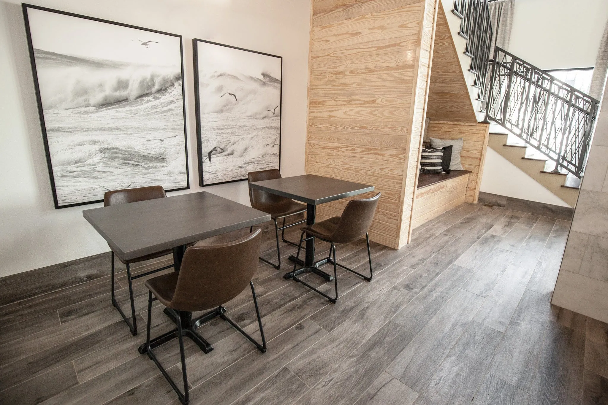 Multifamily amenity nook with two cafe tables and brown leather chairs below oversized black and white surf photographs